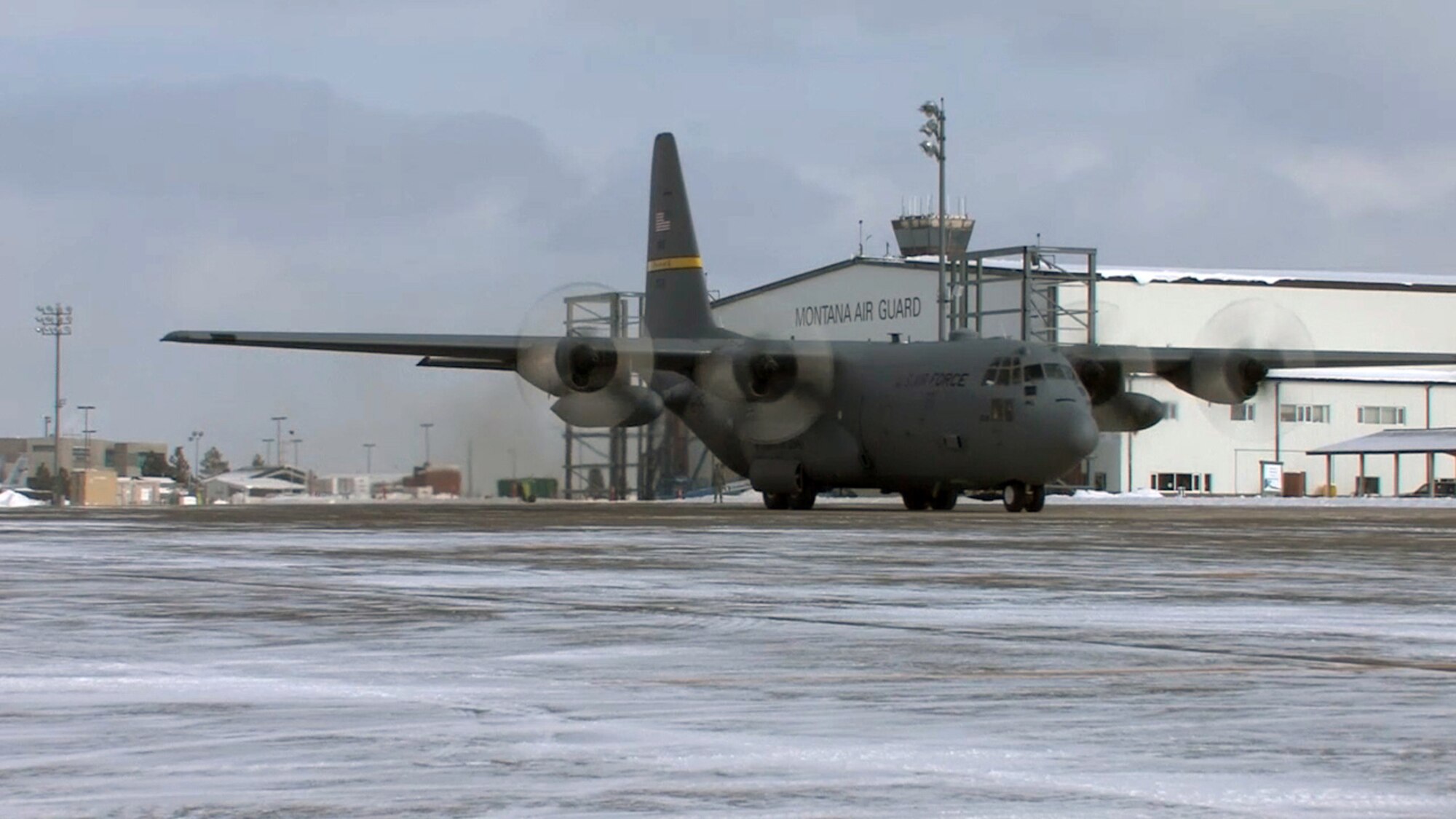 A 153rd Airlift Wing C-130 Hercules cargo aircraft of Wyoming Air National Guard taxis in front of a Montana ANG building at the 120th Fighter Wing, Great Falls, Mont., Feb. 8, 2014. The WY ANG visited the MT ANG to train their personnel in new career fields as the unit transitions from F-16 fighters to C-130 cargo missions. Because the two units experience similar weather Wyoming personnel were able to give advice on what it is like to fly missions in windy, cold conditions. (U.S. Air Force photo extracted from video by Senior Airman Nik Asmussen)
