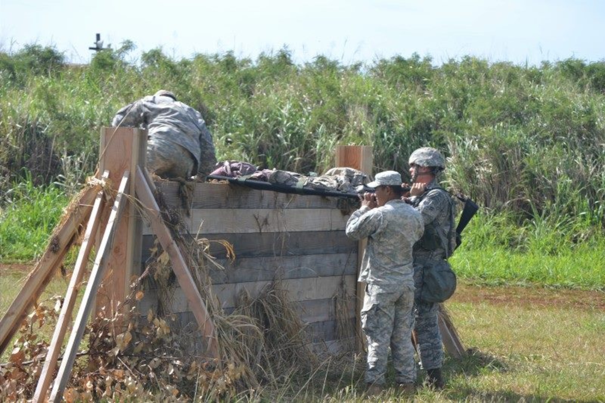 An Airman and Soldier Expert Field Medical Badge course candidates lift a litter over a wall during the EFMB course at Schofield Army Barracks, Hawaii, March 31 through April 11, 2014. The wall was one of two litter obstacles the candidates were tasked to complete. To successfully complete the course, students had to demonstrate their proficiency at tactical combat casualty care, standard and non-standard evacuation operations, take a written test, execute U.S. Army Warrior communications and chemical, biological, radiological, nuclear and high-yield explosives tasks, perform day and night land navigation and complete a 12-mile road march. (U.S. Army photo courtesy of 25th Infantry Division)