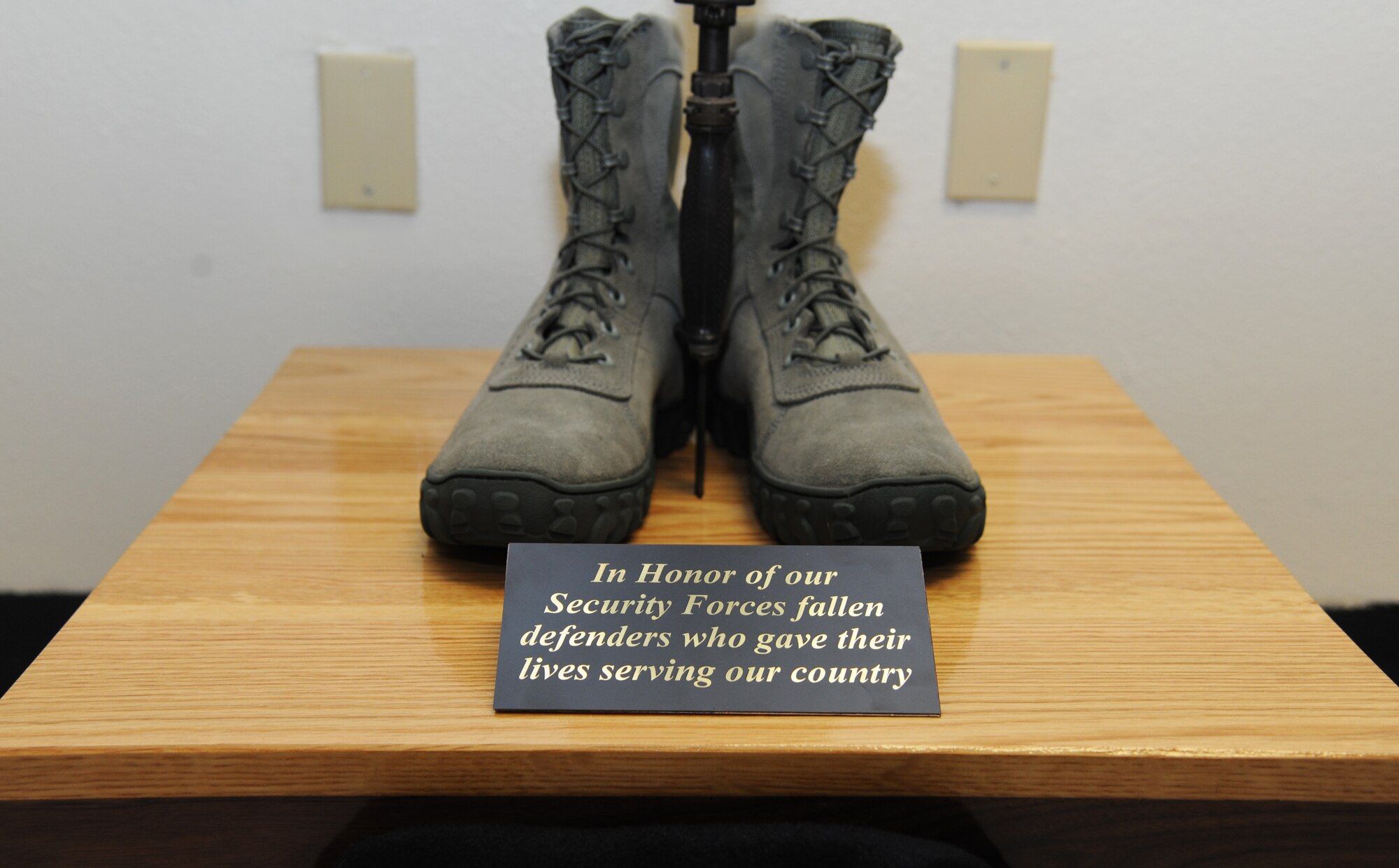 A pair of boots sit at the base of a “fallen soldier battlefield cross,” which also consists of a standing rifle with a helmet and dog tags adorning it, during a memorial ceremony honoring the nine security forces Airmen who lost their lives during Operation Iraqi Freedom and Operation Enduring Freedom April 11, 2014, at the 81st Security Forces Squadron building, Keesler Air Force Base, Miss. The ceremony included the unveiling of the memorial and remarks by base leadership and members of the 81st SFS. The biographies of the deceased Airmen are mounted on the wall behind the memorial. (U.S. Air Force photo by Kemberly Groue)
