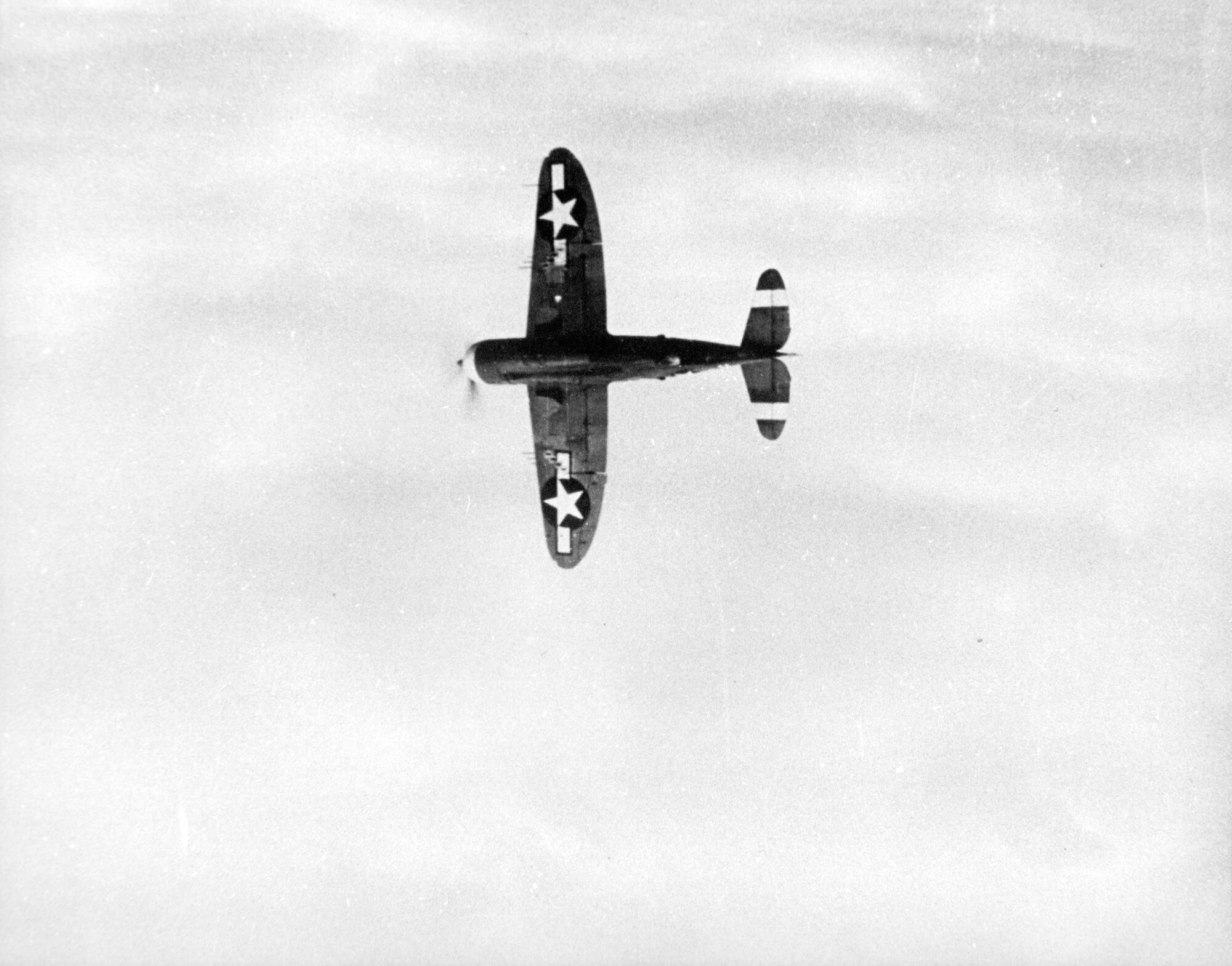 A Republic P-47 Thunderbolt, clean with no bombs or external tanks carried banks away from a camera plane in the European Theater of Operations in World War II.  The national insignia on the bottom of both wings was an ETO measure to help Allied personnel on the ground identify it as a friendly aircraft.  (Source:  142FW History Archives)