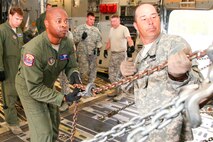 Master Sgt. Eric Walker (second from left), a loadmaster with the 315th Airlift Control Flight at Joint Base Charleston, S.C., teams up with Army Sgt. Brad Calhoun (right) to pull tight on a chain to secure an M1A1SA Abrams main battle tank to the floor of a C-17 Globemaster III Friday at Wright Army Airfield, Ga. C-17's from JB Charleston, S.C., and Wright-Patterson Air Force Base, Ohio, transported four tanks from Wright AAF to McEntire Air National Guard Base, S.C., in support of a tank movement for the 1/118th CAB. (U.S. Air Force photo by Staff Sgt. Rashard Coaxum/released)
