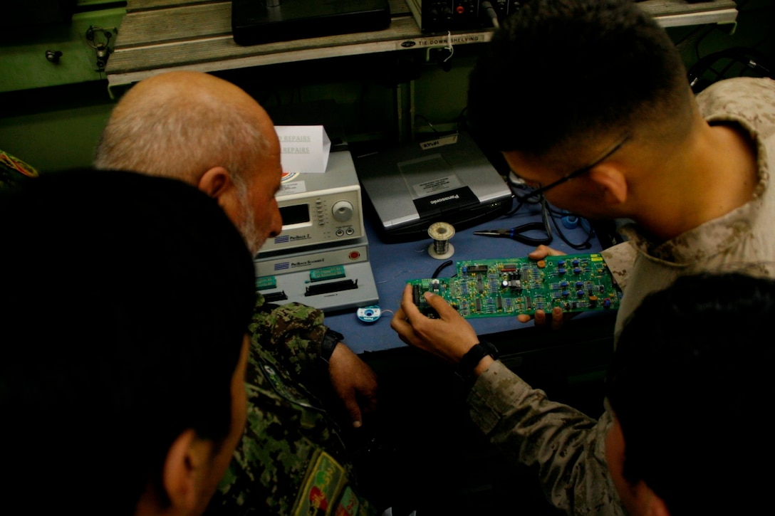 A Marine with Combat Logistics Battalion 7 demonstrates to Afghan National Army soldiers with the 215th Corps how to repair an electronics panel aboard Camp Leatherneck, Helmand province, Afghanistan, April 6, 2014. The period of instruction was part of the curriculum review for the upcoming Communication Electronics Maintenance Course scheduled to begin this month.