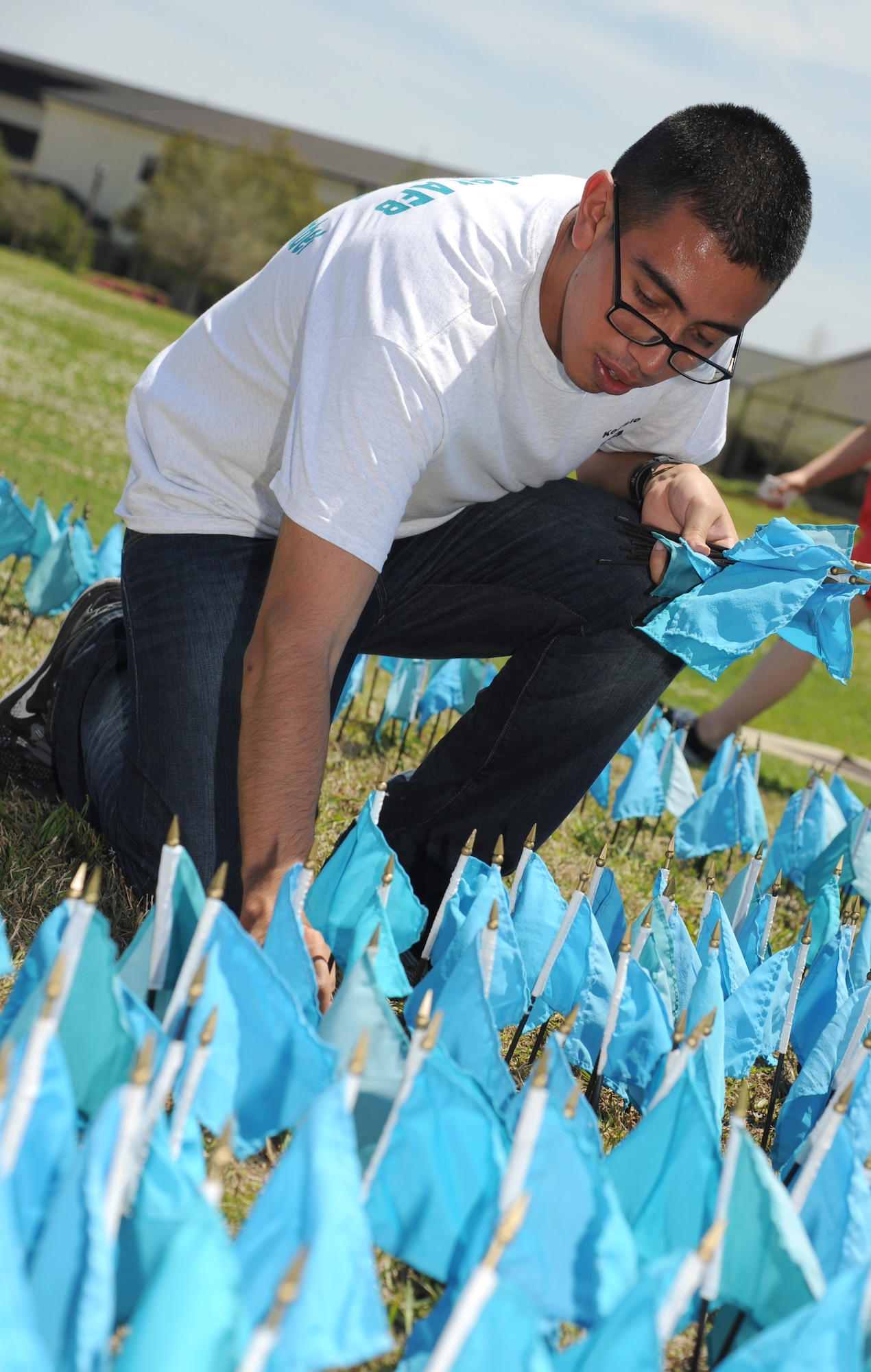 Airman 1st Class Antonio Ruiz, 336th Training Squadron and teal rope member, places teal-colored flags in the ground in the shape of a ribbon for Sexual Assault Awareness Month April 11, 2014 at the triangle parade grounds, Keesler Air Force Base, Miss.  Each flag represents one Air Force member who reported being sexually assaulted in fiscal year 2013.  There are 1,047 flags displayed.  (U.S. Air Force photo by Kemberly Groue)