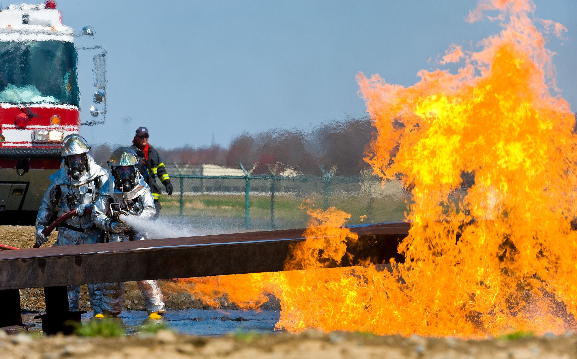 A 436th Civil Engineer Squadron Fire Department two-person fire attack crew aims a stream of water at the left wing of the aircraft fire trainer April 10, 2014, at Dover Air Force Base, Del. Numerous fire attack crews practiced extinguishing flames originating from the flight deck, cargo compartment and wing areas. (U.S. Air Force photo/Roland Balik)