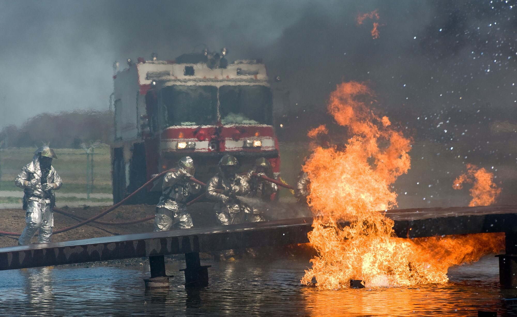 A two-person fire attack crew aims a stream of water on an aircraft fire trainer April 10, 2014, at Dover Air Force Base, Del. Fire attack crews wear aircraft rescue and firefighting proximity gear for protection when battling aircraft fires. (U.S. Air Force photo/Roland Balik)