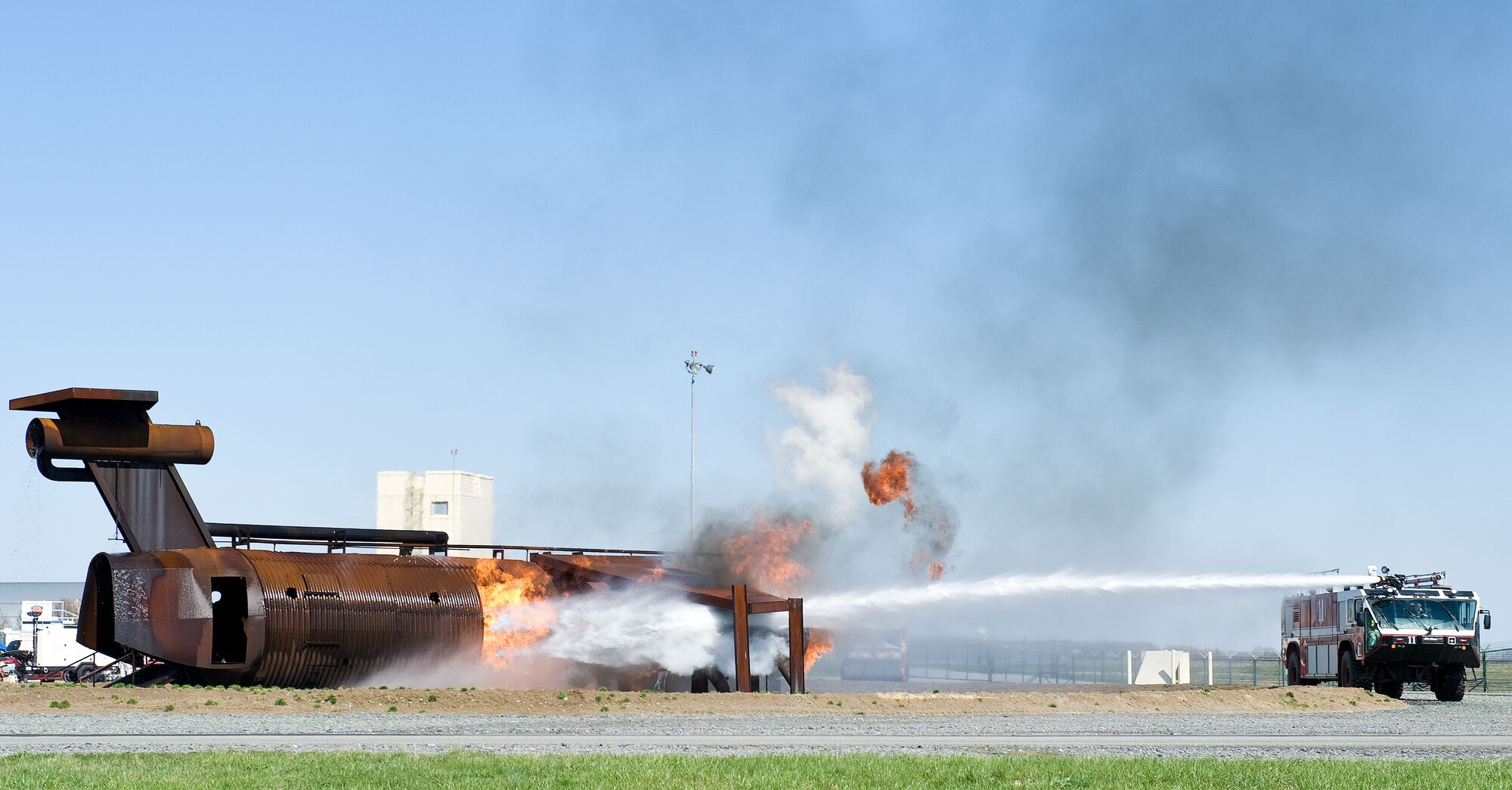 A Striker T-1500 firetruck from the 436th Civil Engineer Squadron Fire Department aims a stream of water at flames engulfing the aircraft fire trainer April 10, 2014, at Dover Air Force Base, Del. Teams of three Fire Dept. personnel took turns in Crash 11 extinguishing flames on the trainer. (U.S. Air Force photo/Roland Balik)