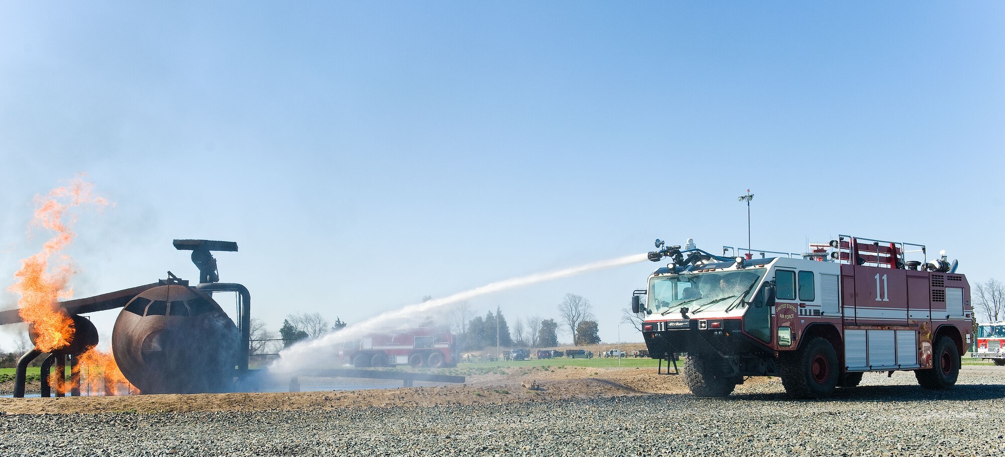 A Striker T-1500 firetruck from the 436th Civil Engineer Squadron Fire Department aims a stream of water at flames engulfing the aircraft fire trainer April 10, 2014, at Dover Air Force Base, Del. Numerous teams of three Fire Dept. personnel took turns in Crash 11 extinguishing flames on the fuselage, flight deck and engines. (U.S. Air Force photo/Roland Balik)