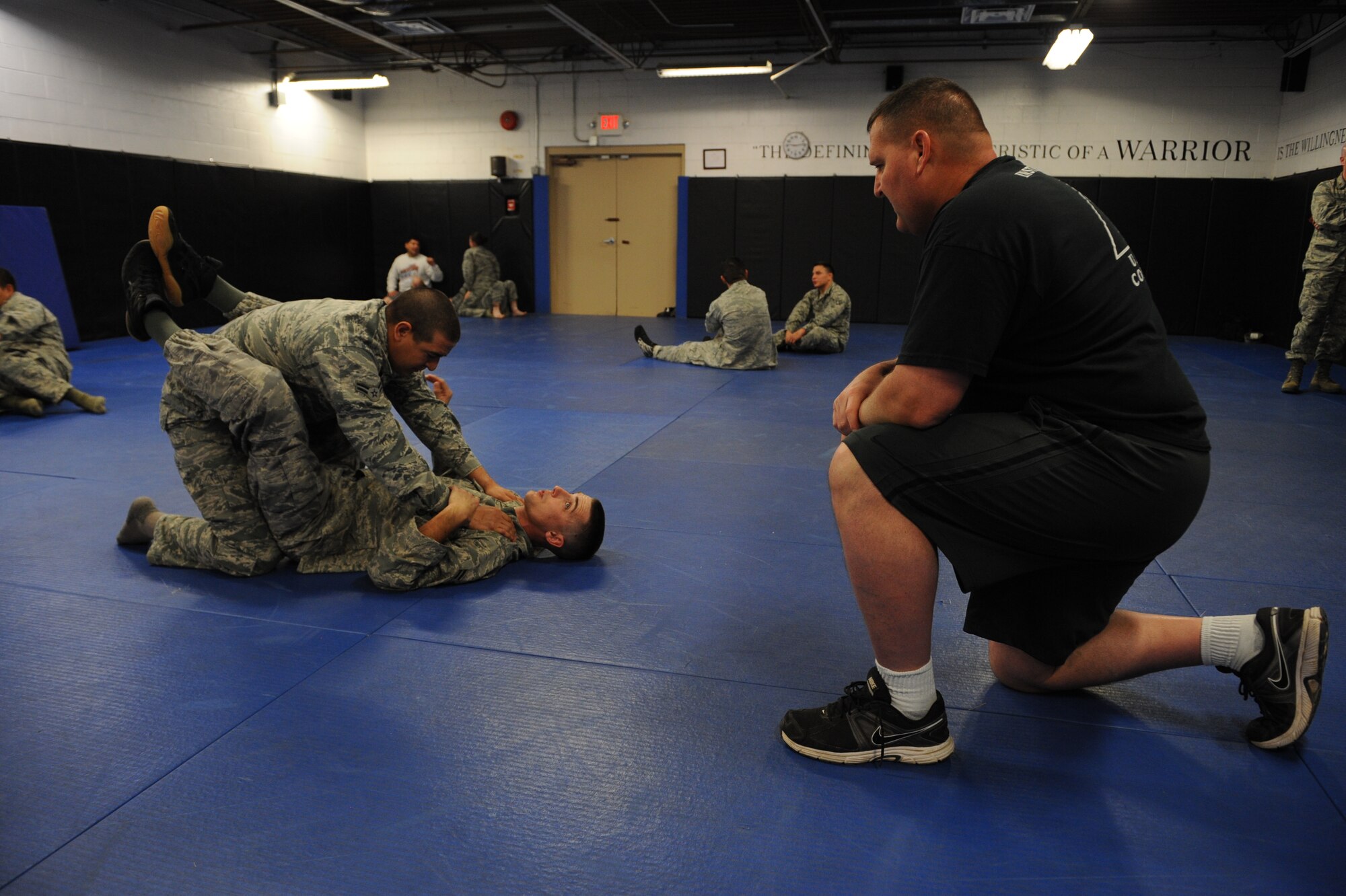 Army instructor Sgt. Major Mark Ruffe observes  Airman 1st Class Stephen Anderson (bottom) forcing Airman 1st Class Jordan Apalategui (top) into a “guard position,” thereby giving Anderson dominancy in the fight. The two security forces specialists were part of an intense 5-day, Army National Guard-instructed training event titled Basic Combative Course at the Western Army National Guard Aviation Training Site gym in Marana, Ariz., March 17-21.