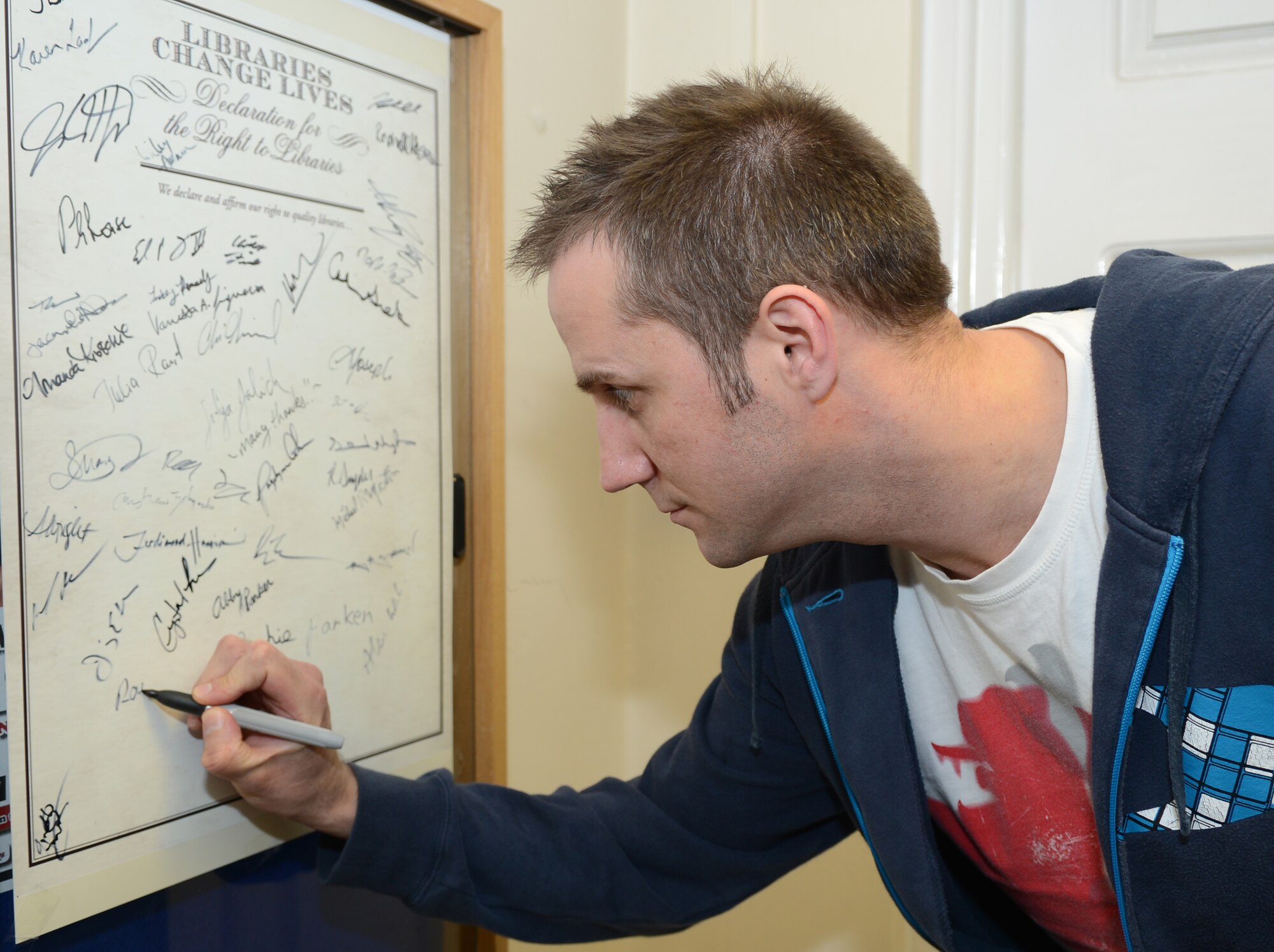 Ray Thompson, 100th Civil Engineer Squadron Electric Shop electrician from Newmarket, England, signs his name on a poster supporting libraries April 15, 2014, at the library on RAF Mildenhall, England. The base library celebrated National Library Week by setting up displays around the building showcasing what the library has to offer and posters with room for people to sign to show their support. This year’s theme for National Library Week is “Libraries Change Lives.” (U.S. Air Force photo by Airman 1st Class Dillon Johnston/Released) 