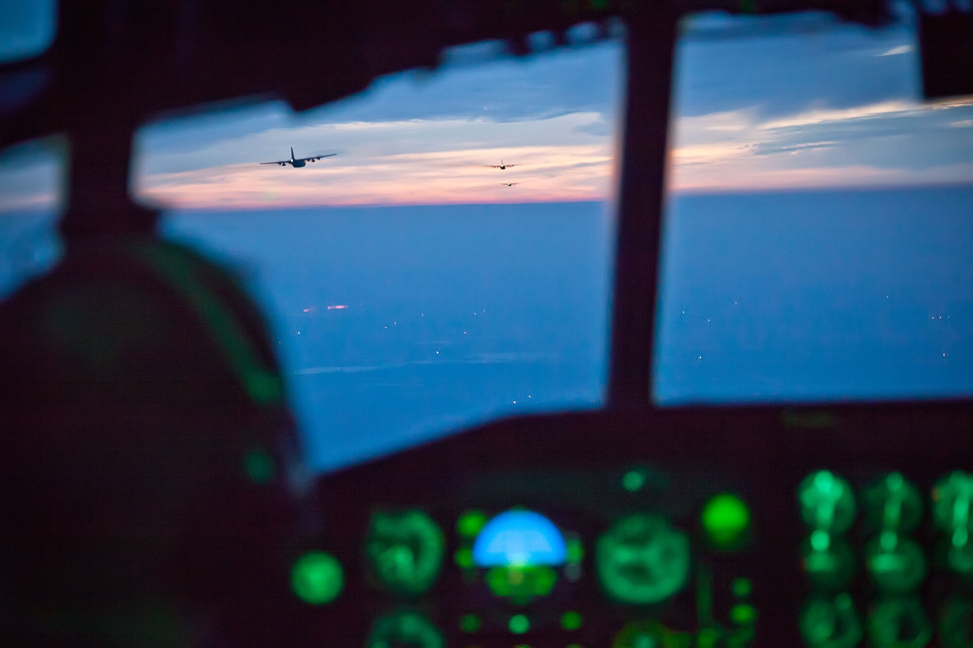 Capt. Andrew Reinhart, 96th Airlift Squadron, watches the first three aircraft in the formation flight as they head into the sunset towards Sioux Falls, S.D., Saturday night. The weekend training missions for the 96th Airlift Squadron and 27th Aerial Port Squadron included preparing and deploying air drops, unscheduled landings, operating in night vision environment and deploying flares.  (U.S. Air Force photo by Shannon McKay/Released)
