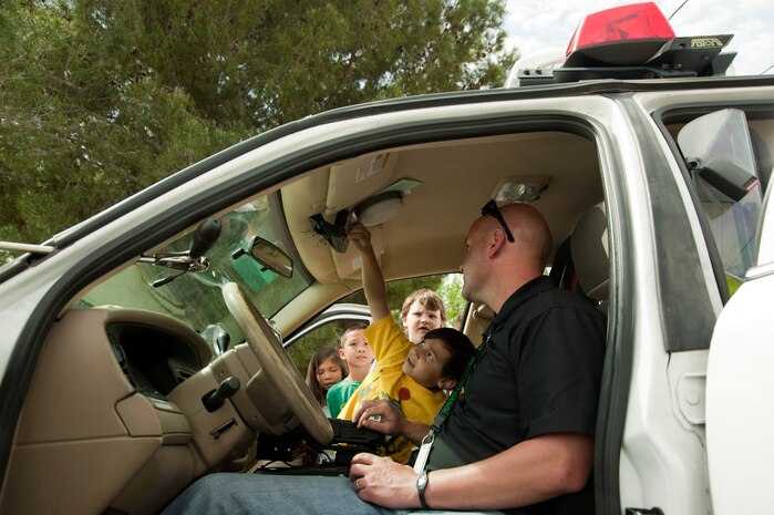 Joe Easterling, Las Vegas Metropolitan Police Department officer observes as Dominic Wallace, Lomie G. Heard Elementary School 1st grade student, operates the patrol car lights April 11, 2014, at Nellis Air Force Base, Nev.  The LVMPD were one of dozens of volunteers present during the school’s career day event. (U.S. Air Force photo by Airman 1st Class Timothy Young)