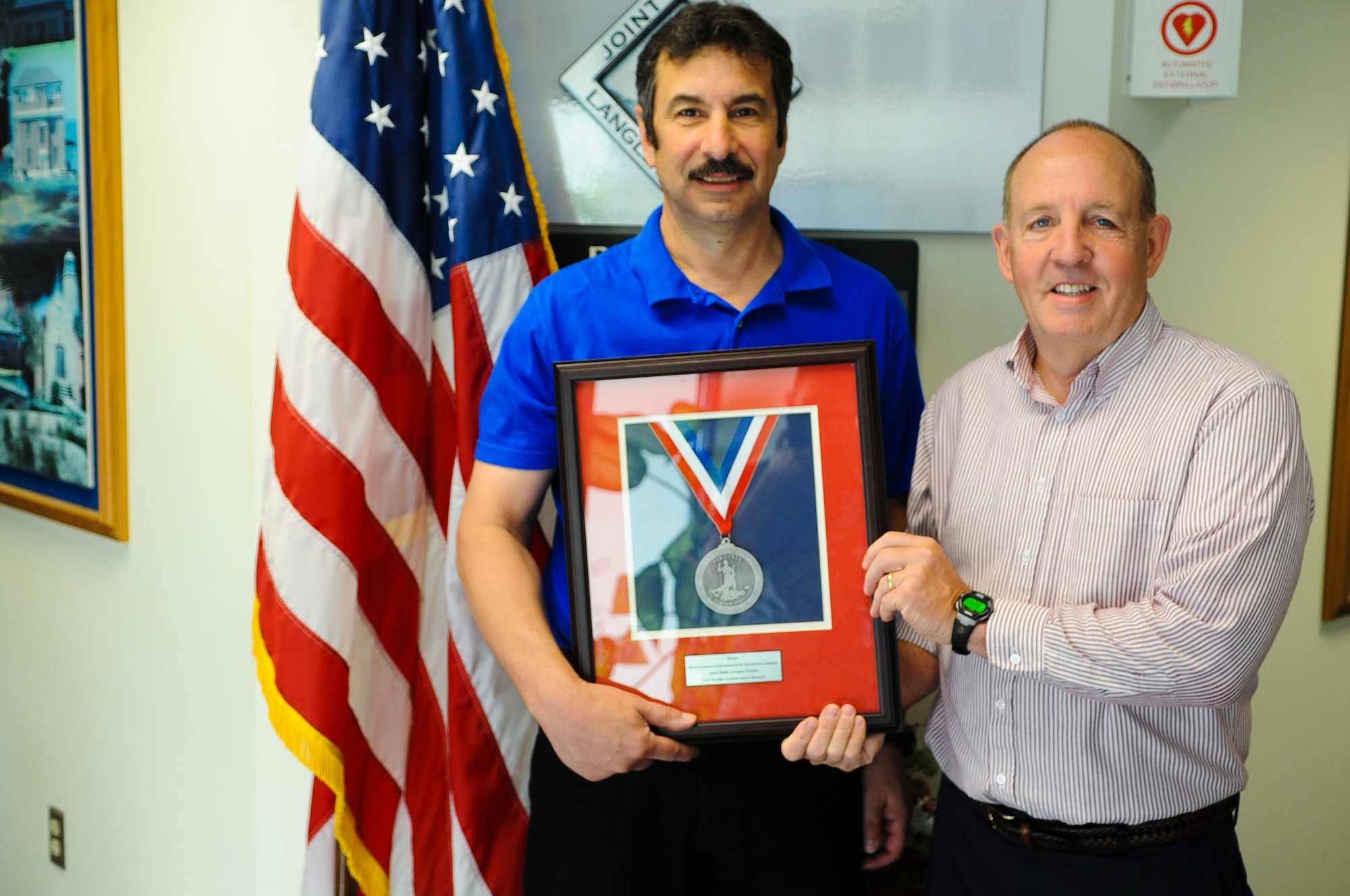 Mark Sciacchitano, 733rd Civil Engineer Division director, and Arba Williamson, 733rd CED pollution prevention specialist, pose for a photograph with the Silver Governor’s Environmental Excellence Award for Conservation at Fort Eustis, Va., April 10, 2014. The 733rd CED won the award for their efforts in protecting Fort Eustis’ cultural and natural assets. (U.S. Air Force photo by Senior Airman Austin Harvill/Released) (photo cropped, sharpened, color corrected and contrasted for effect)