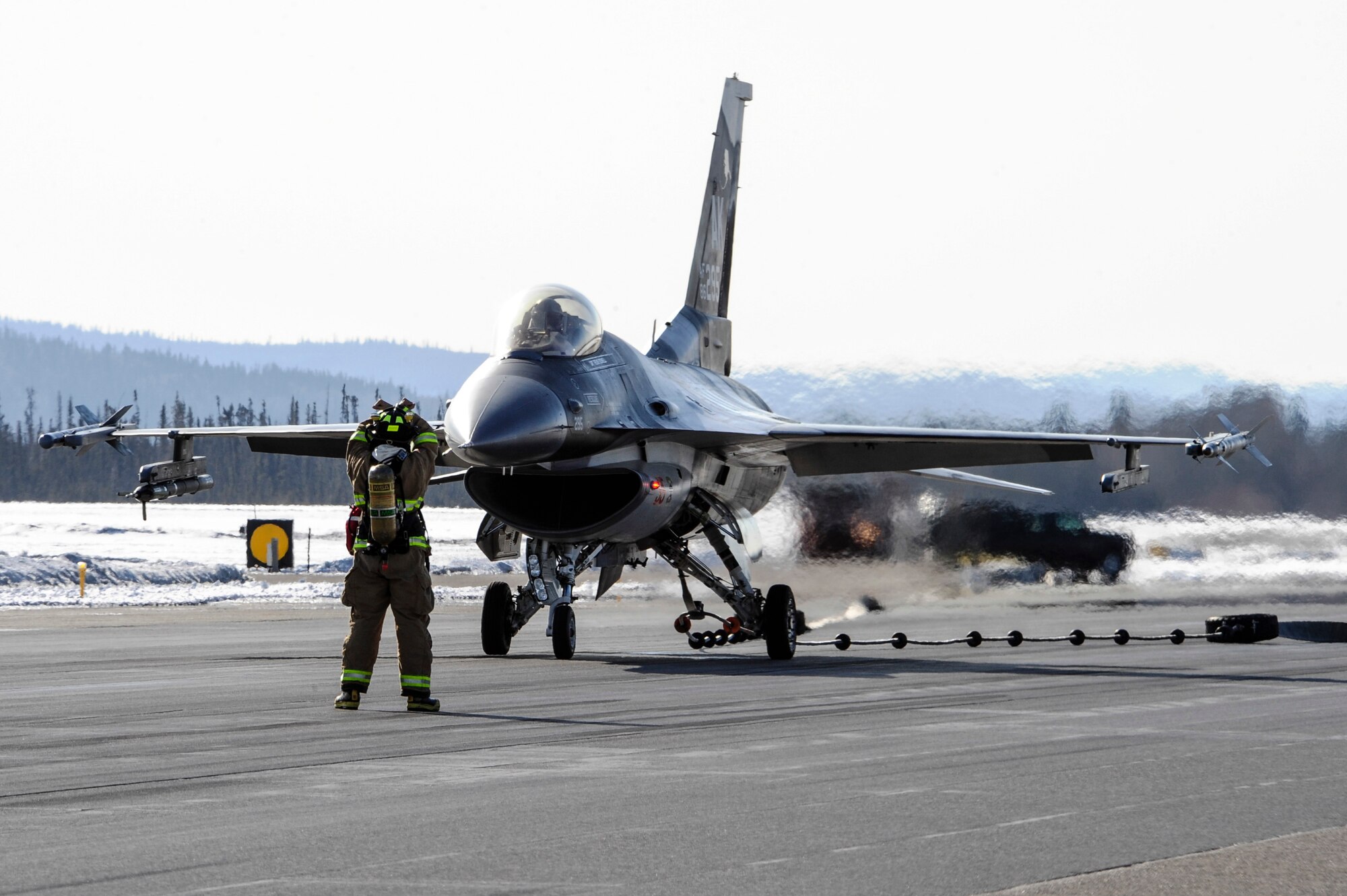 A firefighter with the 354th Civil Engineer Squadron directs an 18th Aggressor Squadron F-16 Fighting Falcon pilot after an arrest-kit cable test April 11, 2014, Eielson Air Force Base, Alaska. The cable system acts as an emergency brake for incoming aircraft which may be experiencing technical difficulties that disable the pilot's ability to land. (U.S. Air Force photo by Senior Airman Zachary Perras/Released)