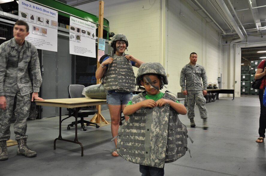 Children don individual protective body armor at the gear issue display at P-1 during Kids Understanding Deployment Operations April 12 at Travis. The children experienced various stations throughout the event that offered face paint, hands on displays of weapons and equipment and tours of static aircrafts. (U.S. Air Force photo/ Staff Sgt. Christopher Carranza)