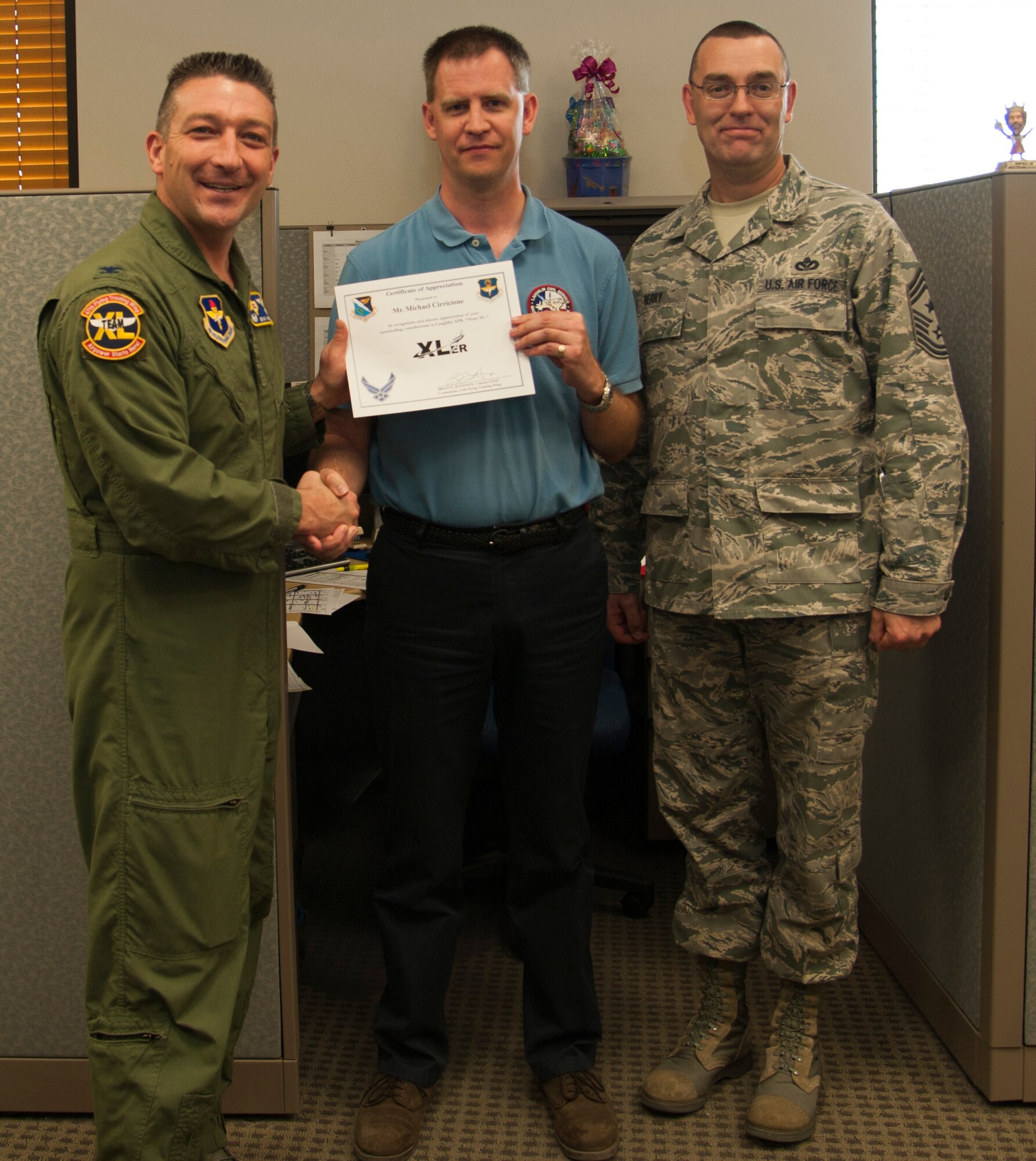 Michael Cirricione, center, 47th Maintenance Directorate T-6 Texan II aircraft scheduler, poses with Col. Brian Hastings, left, 47th Flying Training Wing commander, and Chief Master Sgt. Garry Berry, right, 47th FTW command chief, after being presented the XLer of the week award here April 16, 2014. The XLer is a weekly award chosen by wing leadership and given to those who consistently make outstanding contributions to their unit and Laughlin. (U.S. Air Force photo/Airman 1st Class Jimmie D. Pike/Released)