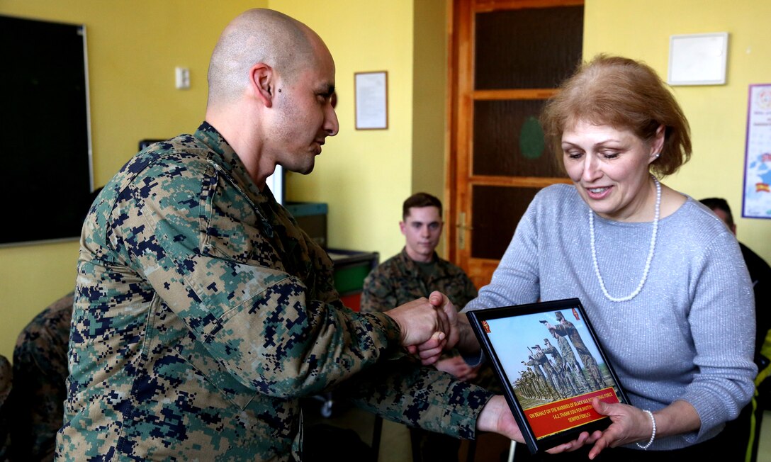 Gunnery Sgt. Damian Rodriguez, the communications chief with 3rd Battalion, 8th Marine Regiment, 2nd Marine Division assigned to Black Sea Rotational Force 14, presents a gift to Ineta Stavavena, the director of the Lejasciems Secondary School in Lejasciems, after talking to students from the school and answering their questions April 9, 2014. The Marines were invited to the school during Summer Shield to speak with children at the school about their experiences in the military, and to answer any other questions they had as well. This is the 11th iteration of the Summer Shield exercise, a joint staff planning and combined arms live fire maneuver event designed to enhance the Latvian Land Force’s capacity and capability to integrate fires and maneuver at the battalion and brigade level as well as increase partner capacity, promote regional stability, and continue to develop Latvian, Lithuanian, Estonian and U.S. interoperability. (Official Marine Corps photo by Lance Cpl. Scott W. Whiting, BSRF PAO/ Released)