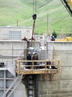 Contractor workers at Little Goose Dam install the new gudgeon arm assembly on the top of the navigation lock’s downstream south gate leaf.