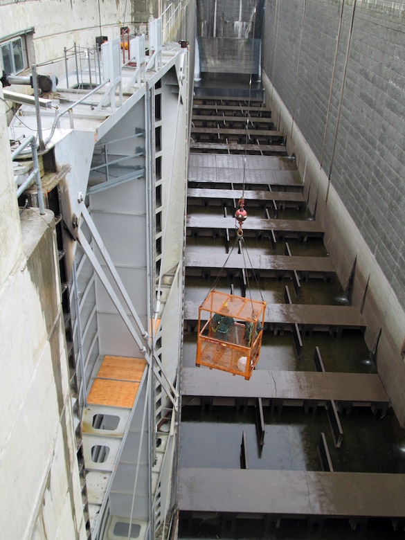 Workers on the gate and in a crane-suspended man basket adjust the diagonal-tensioning nuts on the downstream north navigation lock gate leaf.  Correct tensioning of each gate will help prevent the massive structures from twisting.