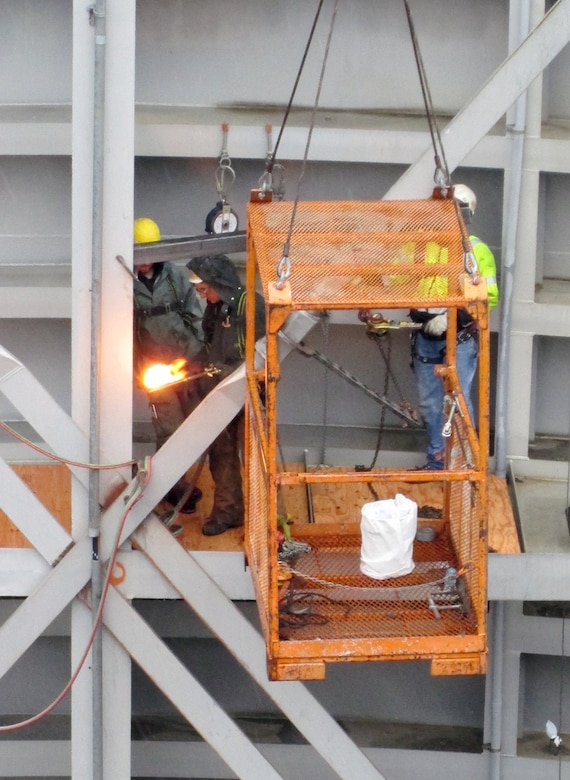 Workers on the gate and in a crane-suspended man basket adjust the diagonal-tensioning nuts on the downstream north navigation lock gate leaf.  Correct tensioning of each gate will help prevent the massive structures from twisting.