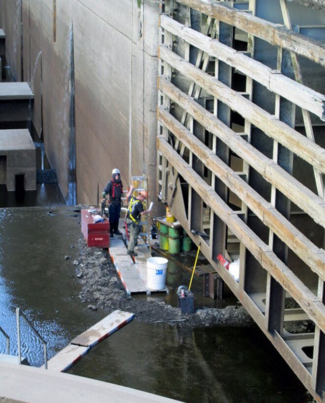 Contractor workers prepare Little Goose Dam’s downstream south navigation lock gate leaf for removing the old, cracked gudgeon assembly. This requires installing retaining brackets on the top, and jacking and shoring equipment under the bottom of the gate to keep it stabile against the navigation lock wall during work.
