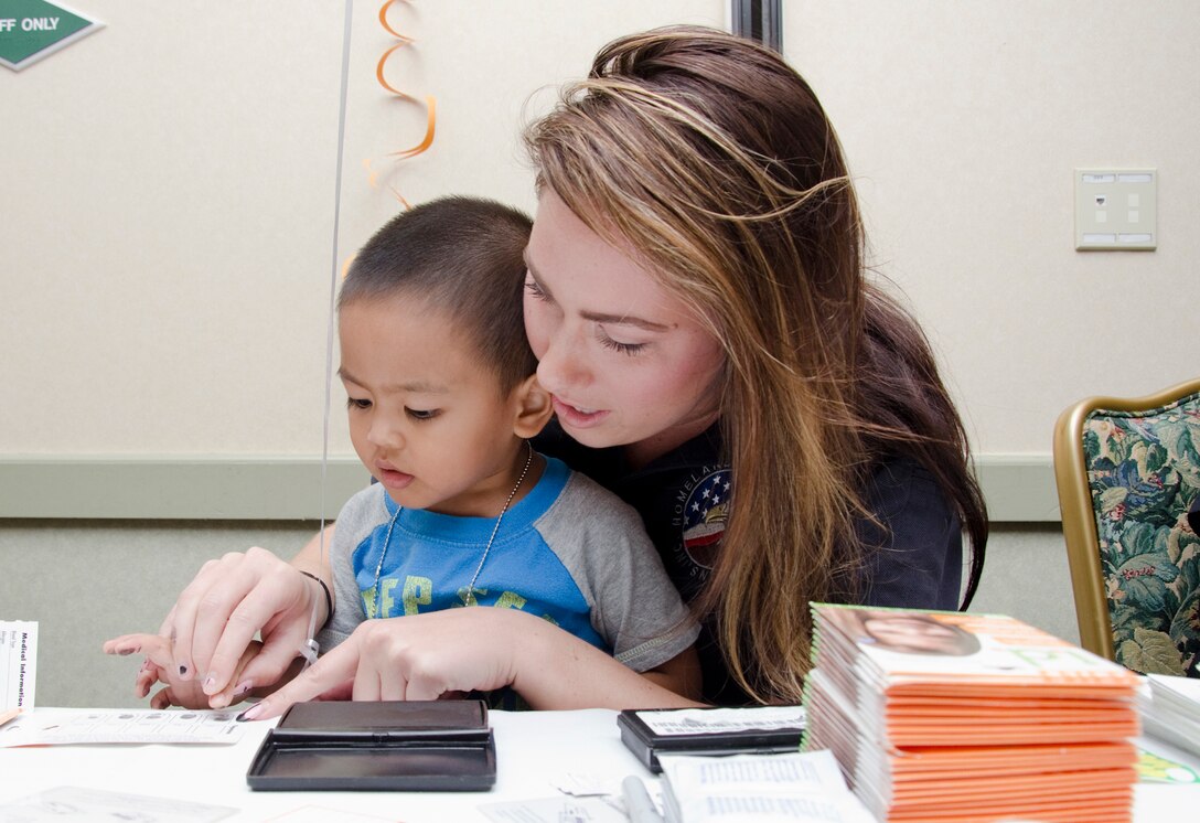 Charity Roden (right), a Provost Marshal’s Office administrative clerk, helps Caeleb Espiritu mark his fingerprints on a special identification card during the Keiki Aloha Expo in the Fairways Ballroom at the Kaneohe Klipper Golf Course, April 11, 2014. (U.S. Marine Corps photo by Kristen Wong)
