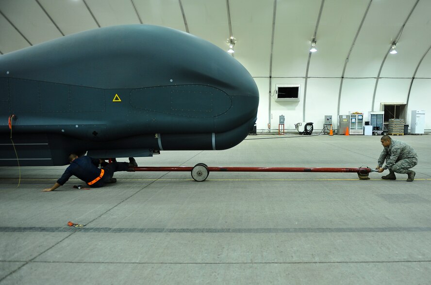 Senior Airman Blaine Aponte and Staff Sgt. Juan Lopez, members of the 380th Expeditionary Aircraft Maintenance Squadron, remove a tow bar from an RQ-4 Global Hawk prior to conducting maintenance operations April 15, 2014, at an undisclosed location in Southwest Asia. The Global Hawk provides intelligence, surveillance, reconnaissance and communications capabilities over Southwest Asia.  (U.S. Air Force photo by Tech. Sgt. Russ Scalf/Released)