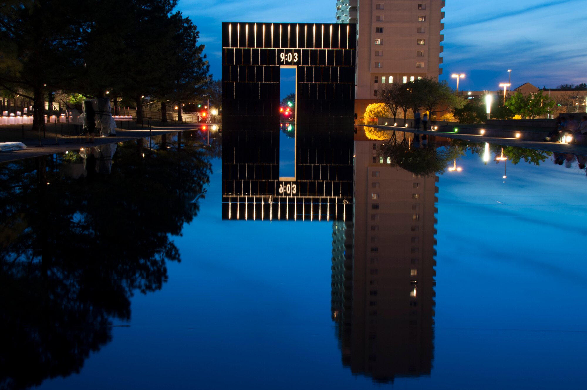 The sun sets on the Oklahoma City Memorial site.  One of the Gates of Time lights up to reveal the moment just after the Alfred P. Murrah Federal Building was bombed.  The site of the Reflecting Pool leading west toward this gate was once N.W. 5th St., with the Murrah Building just to the left.  (U.S. Air Force photo/Senior Airman Mark Hybers)