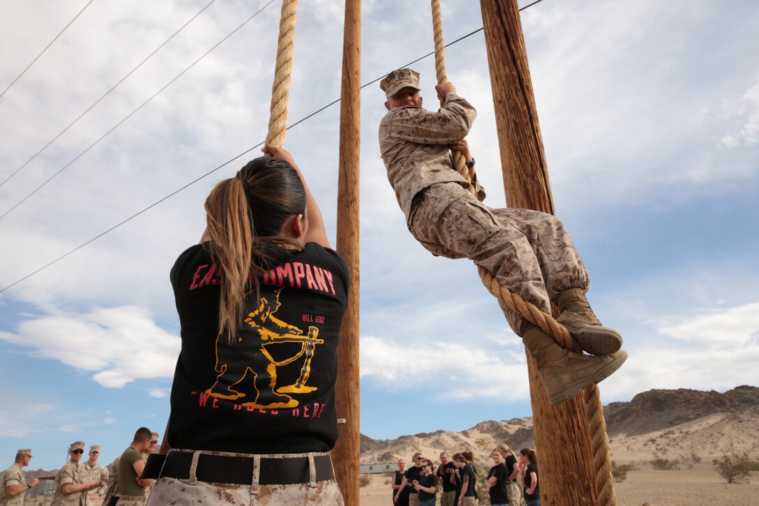Staff Sgt. David Romero, infantry unit leader, 2nd Battalion, 7th Marine Regiment, shows his wife, Nataly Romero, the proper technique for climbing the rope on the obstacle course during 2/7’s Jane Wayne Day, April 11, 2014.
