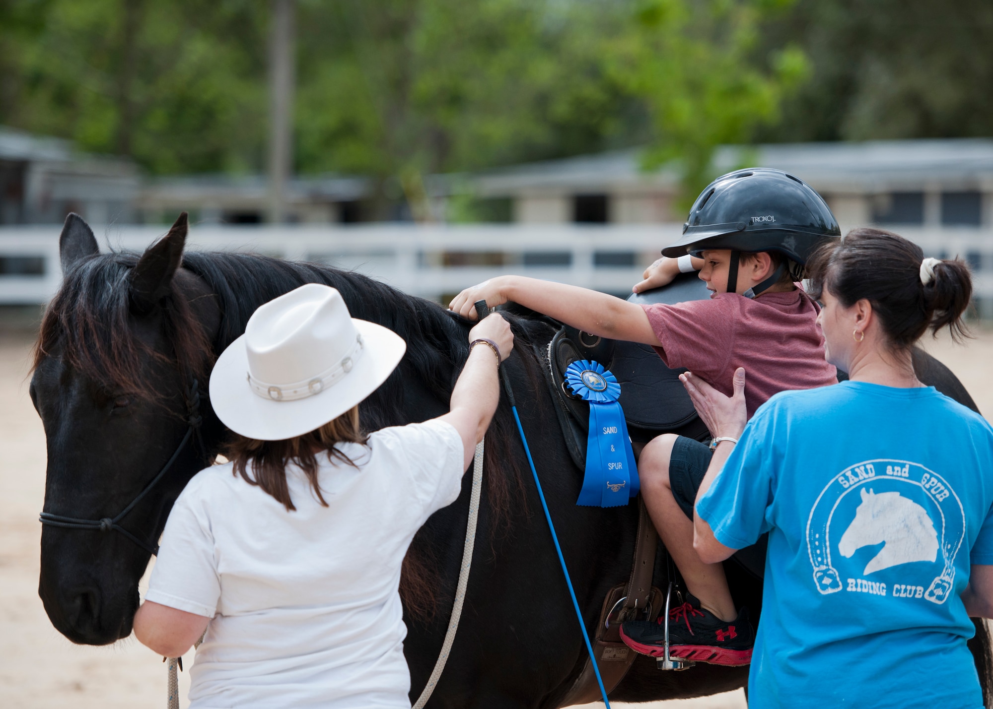 Club members help a new rider climb onto a horse for the first time during the Sand and Spur Riding Club open house event April 19 at Eglin Air Force Base, Fla.  The club provided pony rides for kids and riding and training demonstrations. Those who attended got an up close and hands-on experience with many of the different breeds of horses housed at the stables on base. (U.S. Air Force photo/Samuel King Jr.)
