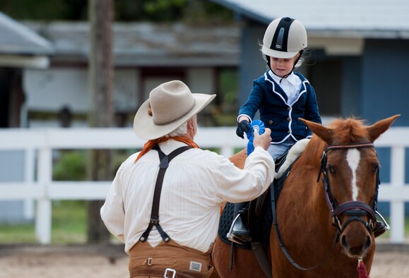 The contest judge presents a blue ribbon to a little rider after a demonstration at the Sand and Spur Riding Club open house event April 19 at Eglin Air Force Base, Fla.  The club provided pony rides for kids and riding and training demonstrations. Those who attended got an up close and hands-on experience with many of the different breeds of horses housed at the stables on base. (U.S. Air Force photo/Samuel King Jr.)