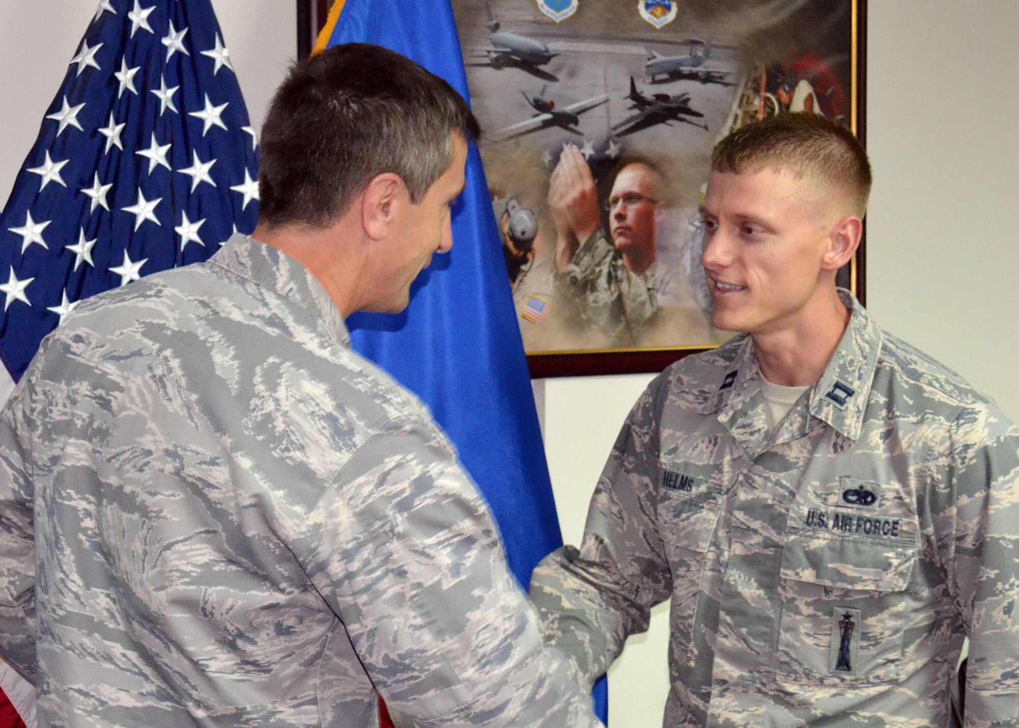 Air Force Brig. Gen. Kevin Schneider, 380th Air Expeditionary Wing commander, presents Air Force Capt. Cory Helms, 380th Mission Support Group executive officer, with his personal coin in recognition of having been awarded the 2014 United States Air Force Leo Marquez Munitions and Missile Maintenance Company Grade Officer of the Year Award.  (U.S. Air Force photo by Maj. Khalid Cannon)