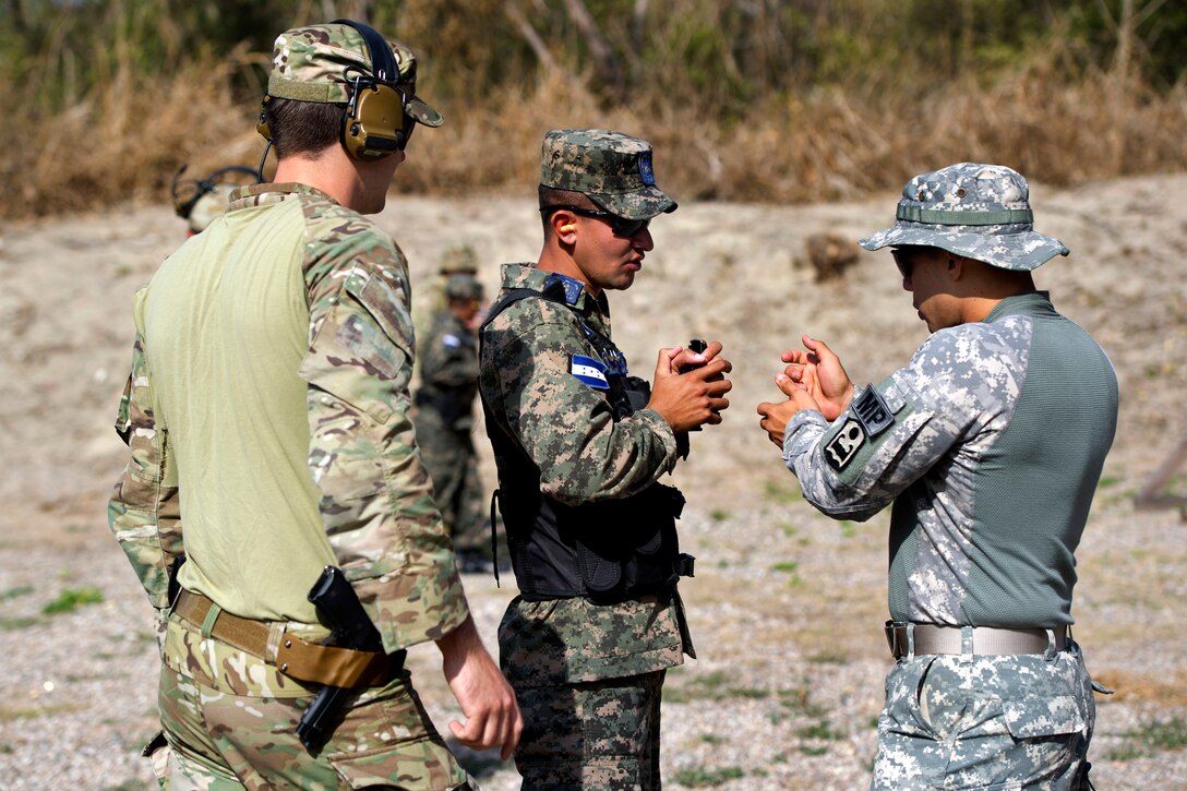 A U.S. Special Forces soldier, left, and U.S. Army specialist Orozco, right, explain how to hold an M9 pistol to a Honduran airman on Soto Cano Air Base, Honduras, April 11, 2014. Orozco is a military policeman assigned to Joint Security Forces on Soto Cano Air Base.