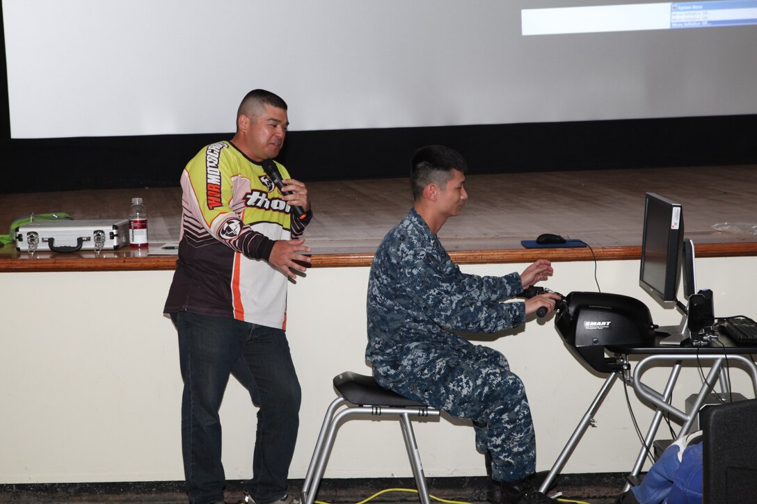 Tsutomu Yamashiro, left, gives feedback while U.S. Navy Petty Officer 2nd Class Hai Dam uses a motorcycle simulator April 18 at the Marine Corps Air Station Futenma Theater during a motorcycle safety stand-down. The simulator displayed various hazards motorcycle riders may encounter and tested their ability to ride and react safely. Yamashiro is a training technician with the Installation Safety Office, and Dam is a corpsman with the U.S. Naval Hospital Okinawa on Camp Foster. 