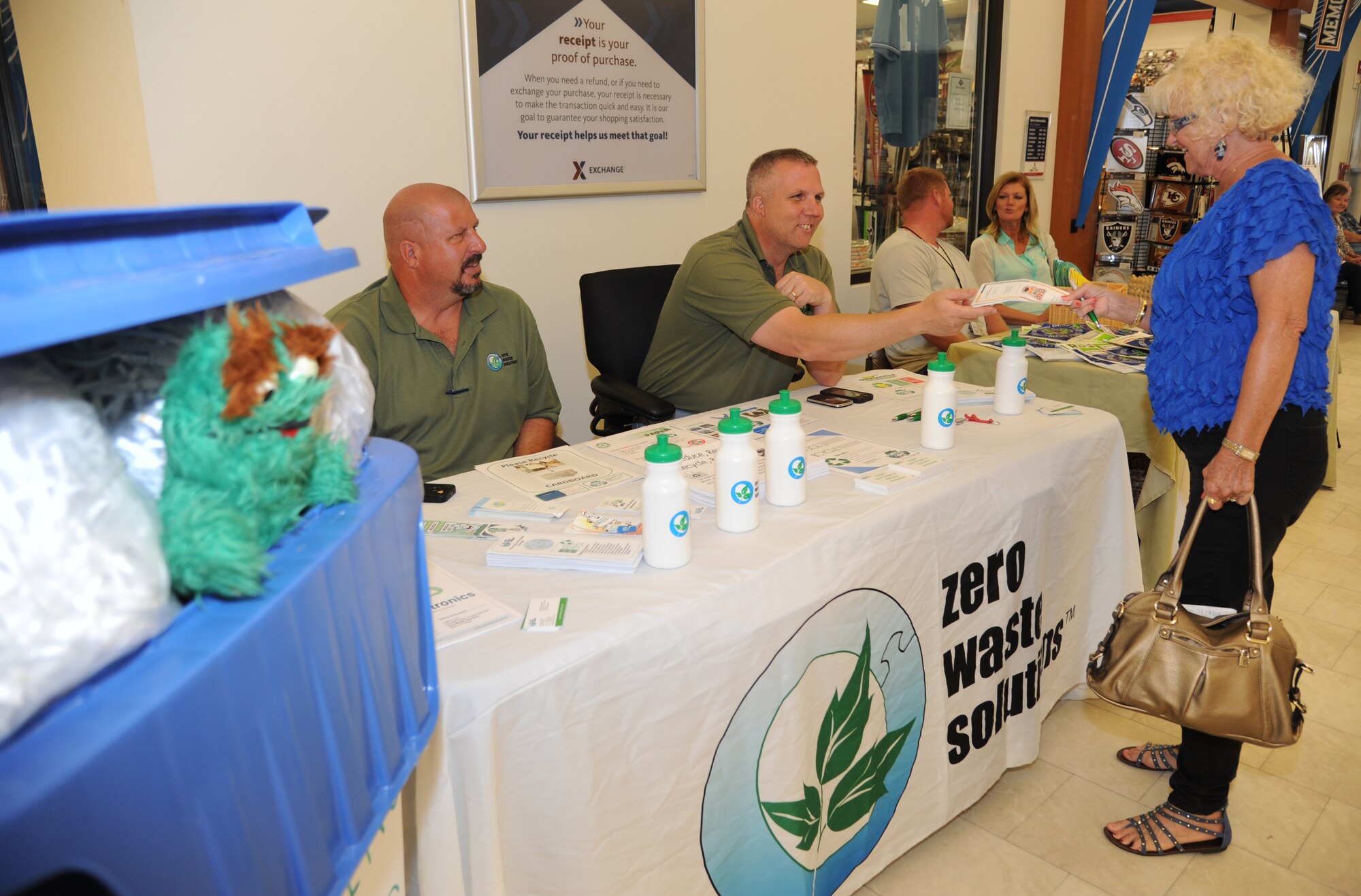 Duane Olsen and Douglas Smith, Zero Waste Solutions, provide an informational recycling pamphlet to Ruth Warnick during her visit to the base exchange April 22, 2014, at Keesler Air Force Base, Miss.  Zero Waste Solutions and PAE/CEV set up booths with hand-outs and literature materials about recycling and environmental sustainability for Keesler personnel in recognition of Earth Day.  (U.S. Air Force photo by Kemberly Groue)