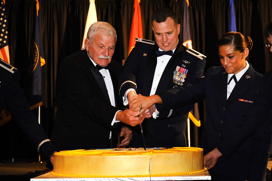 Retired U.S. Air Force Brig. Gen. Regis F.A. Urschler, former 55th Wing commander, U.S. Air Force Col. Gregory Guillot, 55th Wing commander, along with Airman 1st Class Kerrigan Lisis, Communication Security accountant assigned to the 55th Communication Squadron, ceremoniously make the first cut of the Birthday Ball cake at  the Embassy Suites Hotel in LaVIsta, Neb, April 12.  It is tradition for the acting commander of the 55th to cut the cake alongside the youngest Airman in the room as well as a previous wing commander, representing the past, present and future.  (U.S. Air Force photo by Josh Plueger/Released)