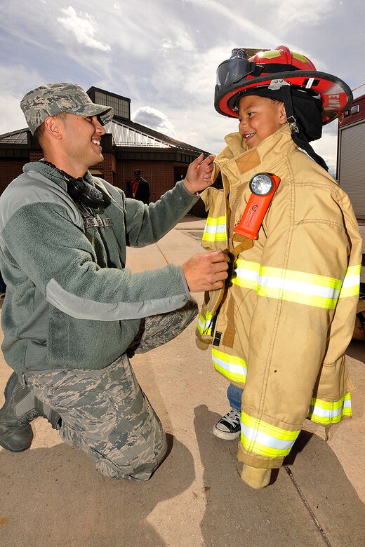 PETERSON AIR FORCE BASE, Colo. – Staff Sgt. Chase Flores, 21st Civil Engineer Squadron fire protection technician, helps Keion Roberts don a fireman’s coat at the Peterson Child Development Center April 15. The demonstration was part of April’s Month of the Military Child observance. (U.S. Air Force photo/Dennis Howk)