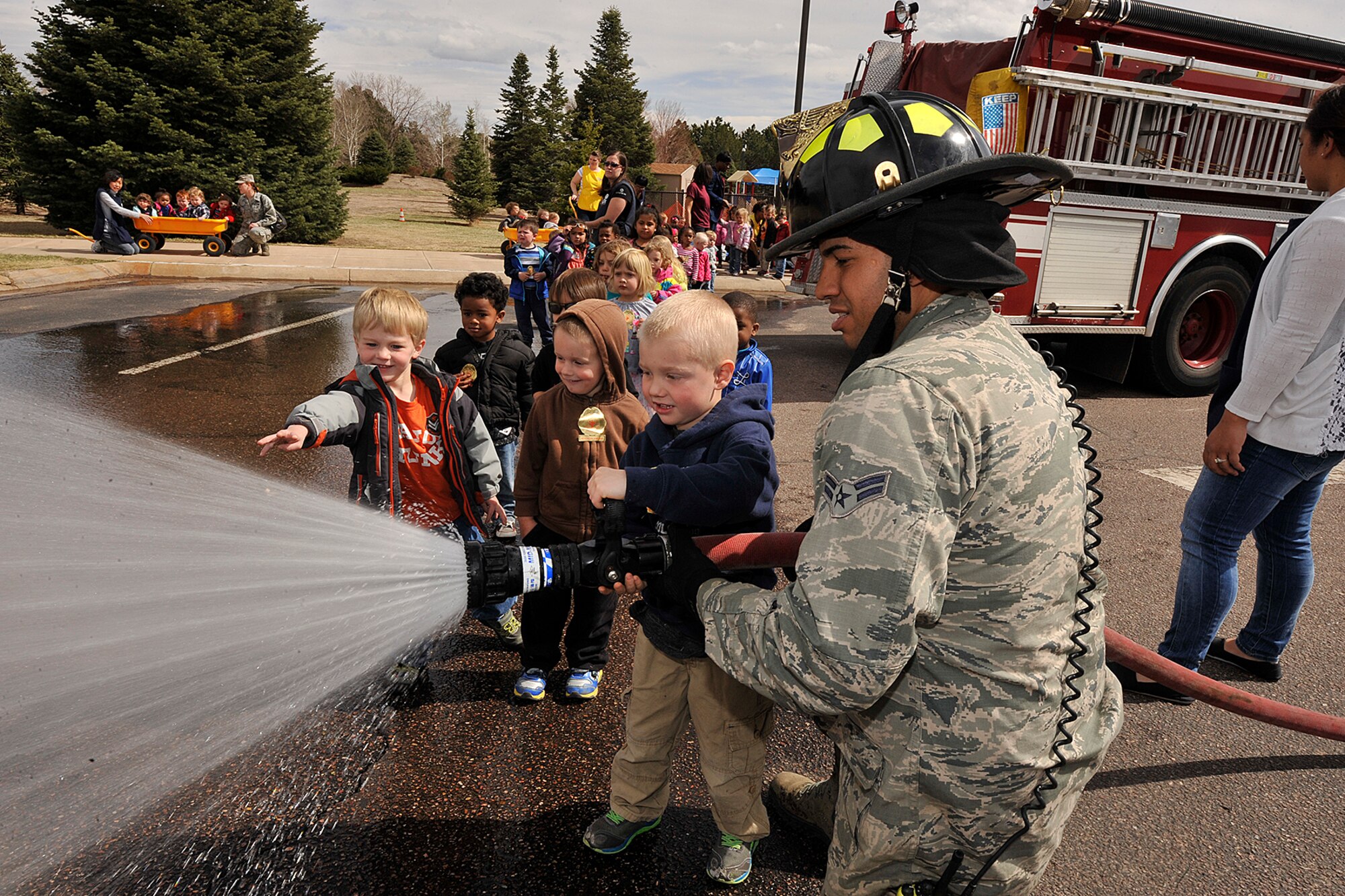 PETERSON AIR FORCE BASE, Colo. – Airman 1st Class Rodolfo Amaya, 21st Civil Engineer Squadron fire protection technician, helps Jason Long spray a fire hose at the Peterson Child Development Center April 15. The demonstration was part of April’s Month of the Military Child observance. (U.S. Air Force photo/Dennis Howk)