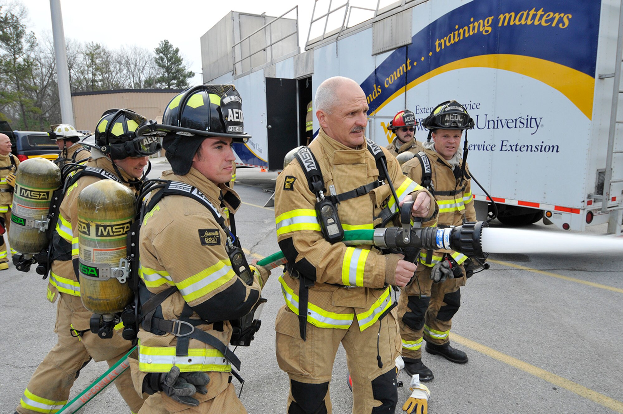 During a recent visit to Arnold Engineering Development Complex (AEDC), Air Force Test Center Commander Maj. Gen. Arnold Bunch (third from left) prepares for live structure fire training with AEDC Firefighter Brandon Gunn (second from left). Gunn explains the operation of the variable stream fog nozzle to Bunch before training in the West Virginia University Fire Service Extension Service mobile burn trailer. Bunch, in full protective clothing, deploys a 1.75-inch hose line to combat multiple propane fueled fires in a smoke filled environment capable of reaching temperatures in excess of 1,200 degrees Fahrenheit. The purpose of the demonstration was to give the commander a greater sense of the demanding environment firefighters face during emergency operations. AEDC firefighters John Templeton (left) and AEDC Fire Department Driver Operator Ken Locker (right) also participate in the training. (Photo by Rick Goodfriend)
