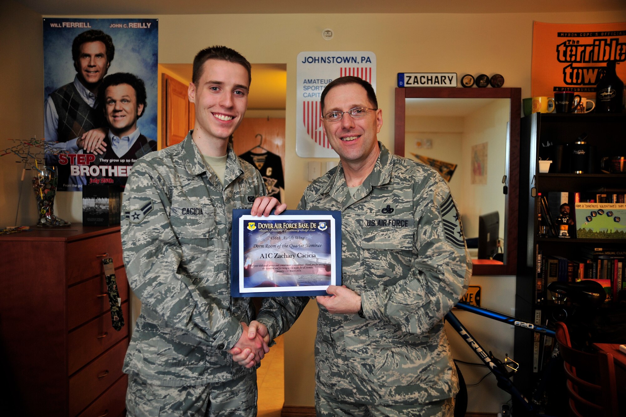 Chief Master Sgt. Stanley C.P. Cadell, 436th Airlift Wing command chief, right, presents a Dorm Room of the Quarter Nominee certificate to Airman 1st Class Zachary Cacicia, 436th AW Public Affairs photojournalist, April 10, 2014 at Dover Air Force Base, Del. Cadell began his tour as the Eagle Wing's command chief in March of this year. (U.S. Air Force photo/Staff Sgt. Elizabeth Morris)