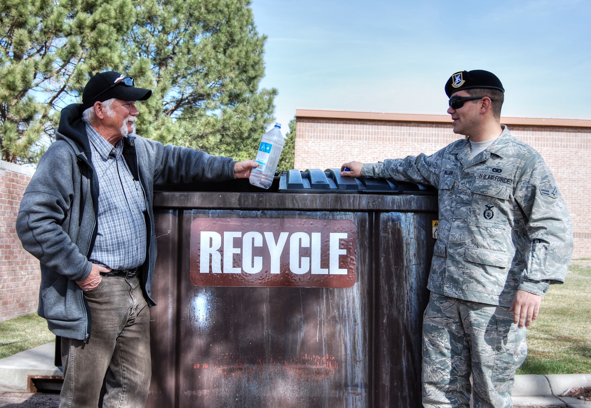 PETERSON AIR FORCE BASE, Colo. – Phil Chase, 21st Civil Engineer Squadron pollution prevention manager (left) and Airman 1st Class Alex Smalldon, 21st Security Forces Squadron reports and analysis, stand near the recycling dumpster outside of building 590. More than 250 individual single stream recycling bins have been placed throughout four separate dorm buildings, making it easier and more convenient for Team Pete members to participate in the base-wide recycling effort. (U.S. Air Force photo/Michael Golembesky)