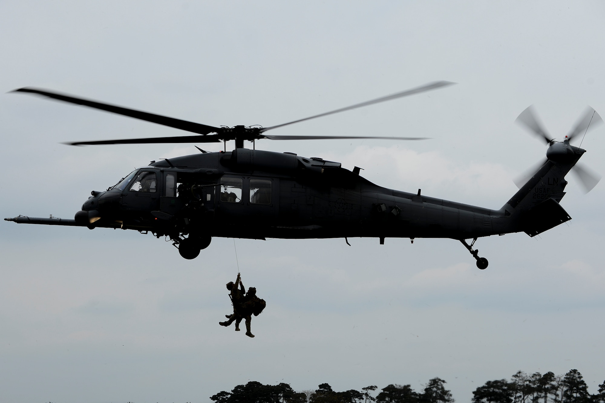Chief Master Sgt. Chad Clark, 56th Rescue Squadron superintendent, and Maj. Patrick Gruber, 56th RQS director of operations, hang from an HH-60G Pave Hawk after the successful recovery of a mock crash victim during a combat search and rescue exercise at Royal Air Force Lakenheath, England, April 17, 2014. The rescue mission scenario included pararescue and security forces teams recovering a victim injured by an improvised explosive device. (U.S. Air Force photo by Airman 1st Class Trevor T. McBride/Released)