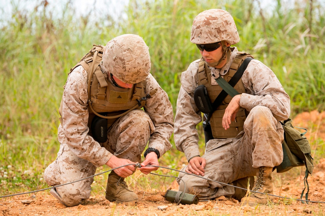 Lance Cpl. James E. Brown, left, ties detonation cord while Cpl. Andrew D. Hoisington supervises during a four-day basic demolition course at Camp Schwab April 15, 2014. The Marines placed blocks of TNT in an interconnected ring of detonation cord, helping to create what is known as a “TNT ring main.” Brown is a combat engineer currently serving as a civil affairs noncommissioned officer with the civil affairs detachment, G-3, operations, III Marine Expeditionary Force. Hoisington is a combat engineer with Marine Wing Support Squadron 172, Marine Aircraft Group 36, 1st Marine Aircraft Wing, III MEF. 