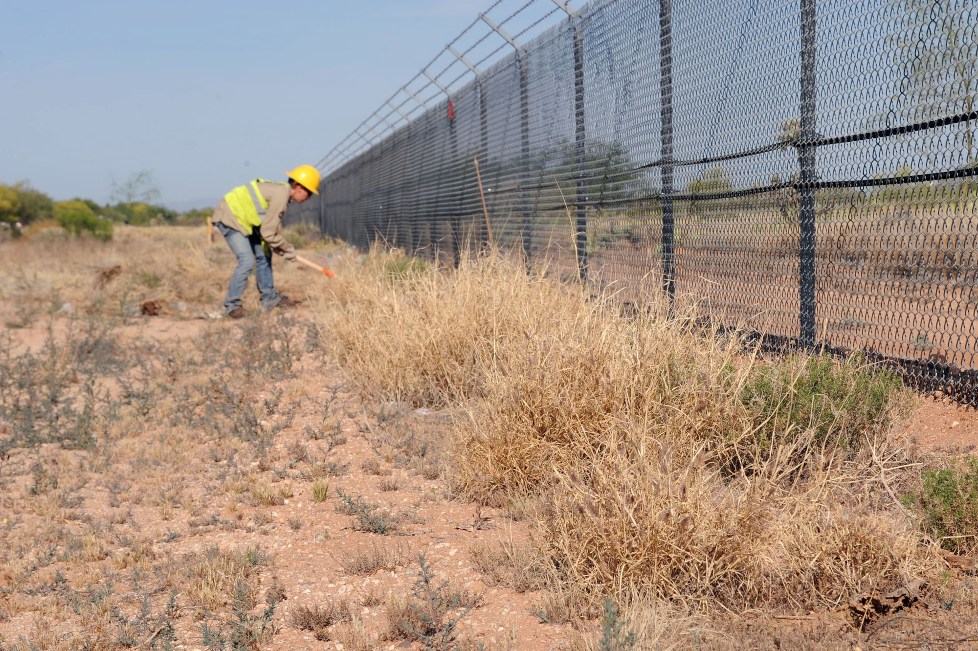 Lesley Burkes, Arizona Conservation Corps crew member, removes buffelgrass outside the fence line at Davis-Monthan Air Force Base, Ariz., April 22, 2014. Buffelgrass is highly flammable and produces a thick black smoke when on fire. The dark smoke can limit aircraft visibility which can also lead to flight line closure. (U.S. Air Force photo by Airman 1st Class Cheyenne Morigeau/ Released)
