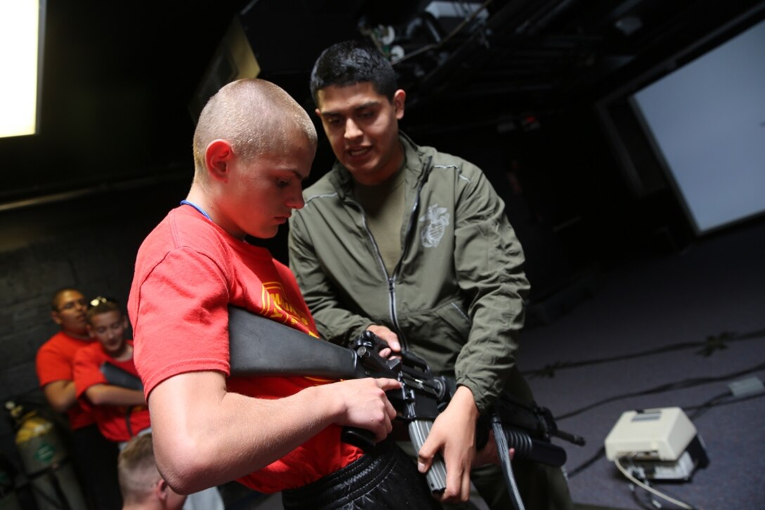Lance Corporal Diomar Guano, range coach on Marine Corps Logistics Base Barstow, Calif., teaches children with the Excelsior High Desert Young Marine program how to shoot weapons on an Indoor Simulated Marksmanship Trainer here, April 12. Active-duty Marines here gave the Young Marines professional military education during their time on MCLB Barstow. 