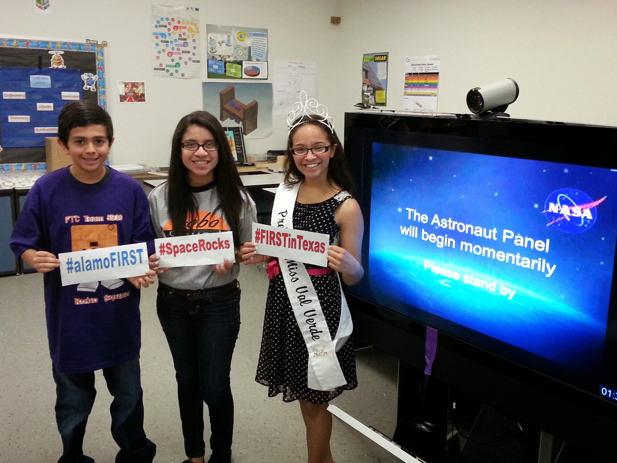 Sammy Sunderland, 12, Jackie Vasquez, 13 and Pre-Teen Miss Val Verde Brianna Marrufo, 14, display hashtags to promote FIRST Robotics through social media prior to the International Space Station downlink at Del Rio Middle School, Del Rio, Texas, April 24, 2014. Sammy, Jackie and Brianna represent the For Inspiration and Recognition of Science and Technology Tech Challenge teams at the middle school and were able to talk to the astronauts living and working at the International Space Station. (Photo courtesy of John Reed)