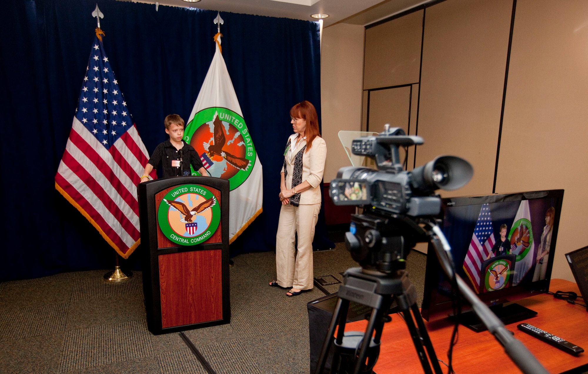 Tamara Parker, U.S. Central Command Communication Integration directorate program manager, educates a child on how to read from a teleprompter to simulate what it’s like to give a media briefing. The simulated media brief and brief on the directorate were available for families during USCENTCOM’s Family Open House at MacDill Air Force Base, Fla., April 18. (U.S. Marine Corps photo by Sgt. Fredrick J. Coleman/Released)