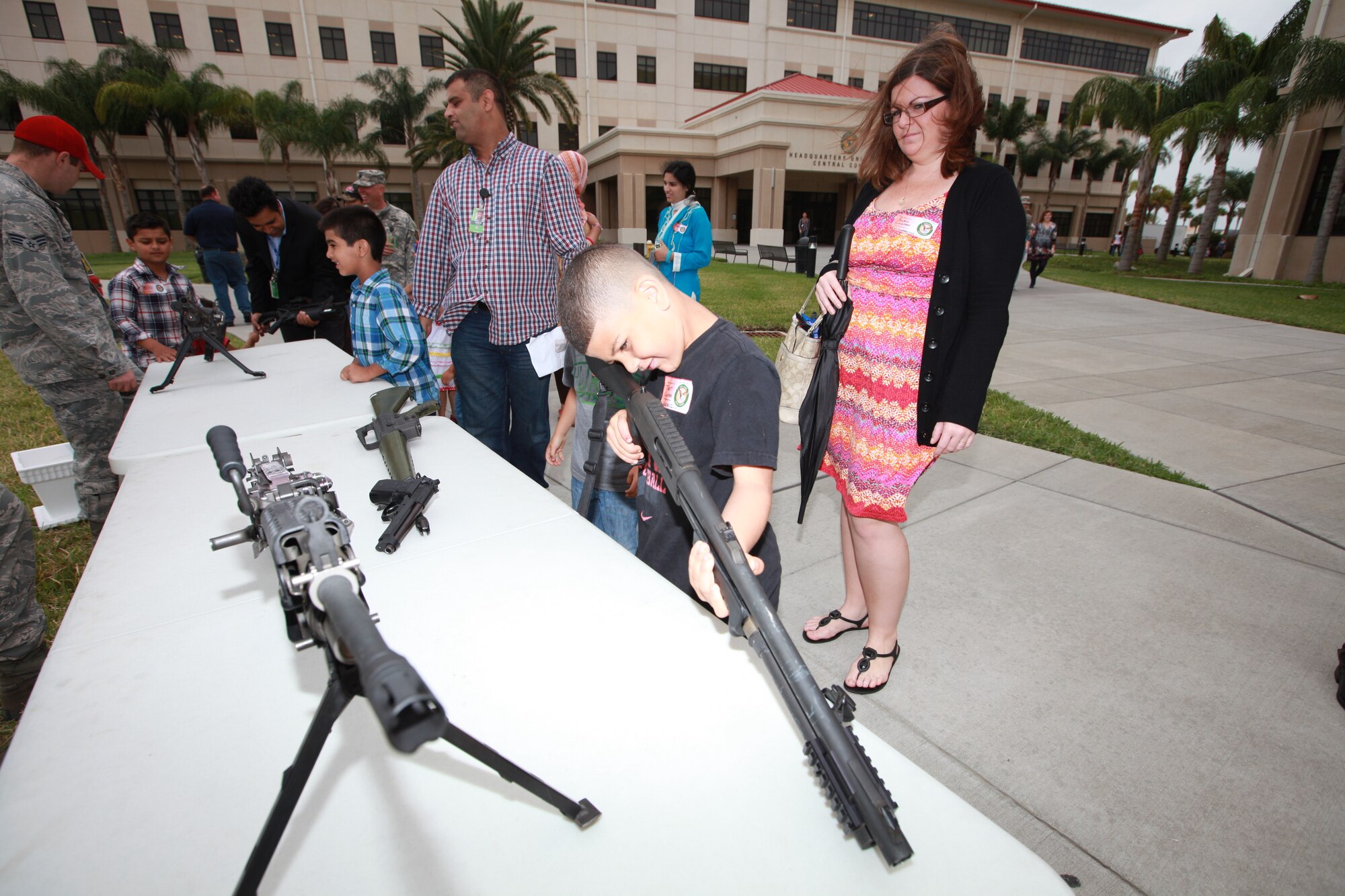 Trent, son of Sgt. Fredrick J. Coleman, U.S. Central Command public affairs, takes aim with a shotgun as his mother Jewell, wife of Sgt. Coleman, looks on at the small arms display during USCENTCOM’s Family Open House at MacDill Air Force Base, Fla., April 18.  (U.S. Marine Corps photo by Sgt. Fredrick J. Coleman/Released)