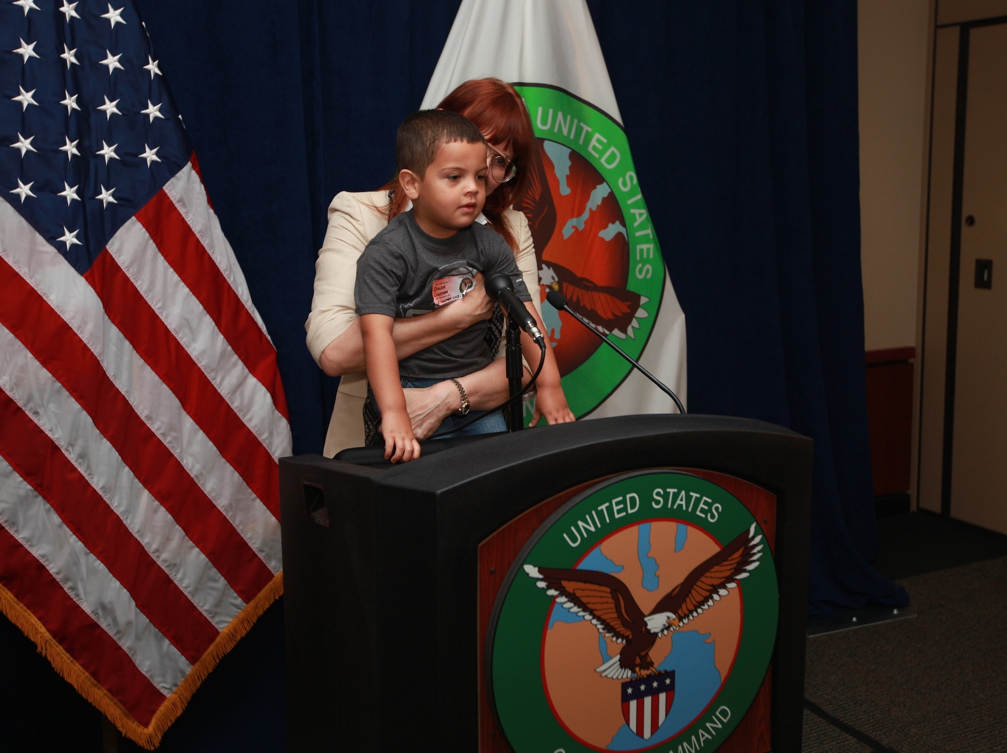 Tamara Parker, U.S. Central Command’s Communication Integration directorate program manager, holds Dylan, son of Sgt. Fredrick J. Coleman, USCENTCOM public affairs, up to the lectern to let him see the camera and teleprompter at the media briefing display during USCENTCOM’s Family Open House at MacDill Air Force Base, Fla., April 18. (U.S. Marine Corps photo by Sgt. Fredrick J. Coleman/Released)