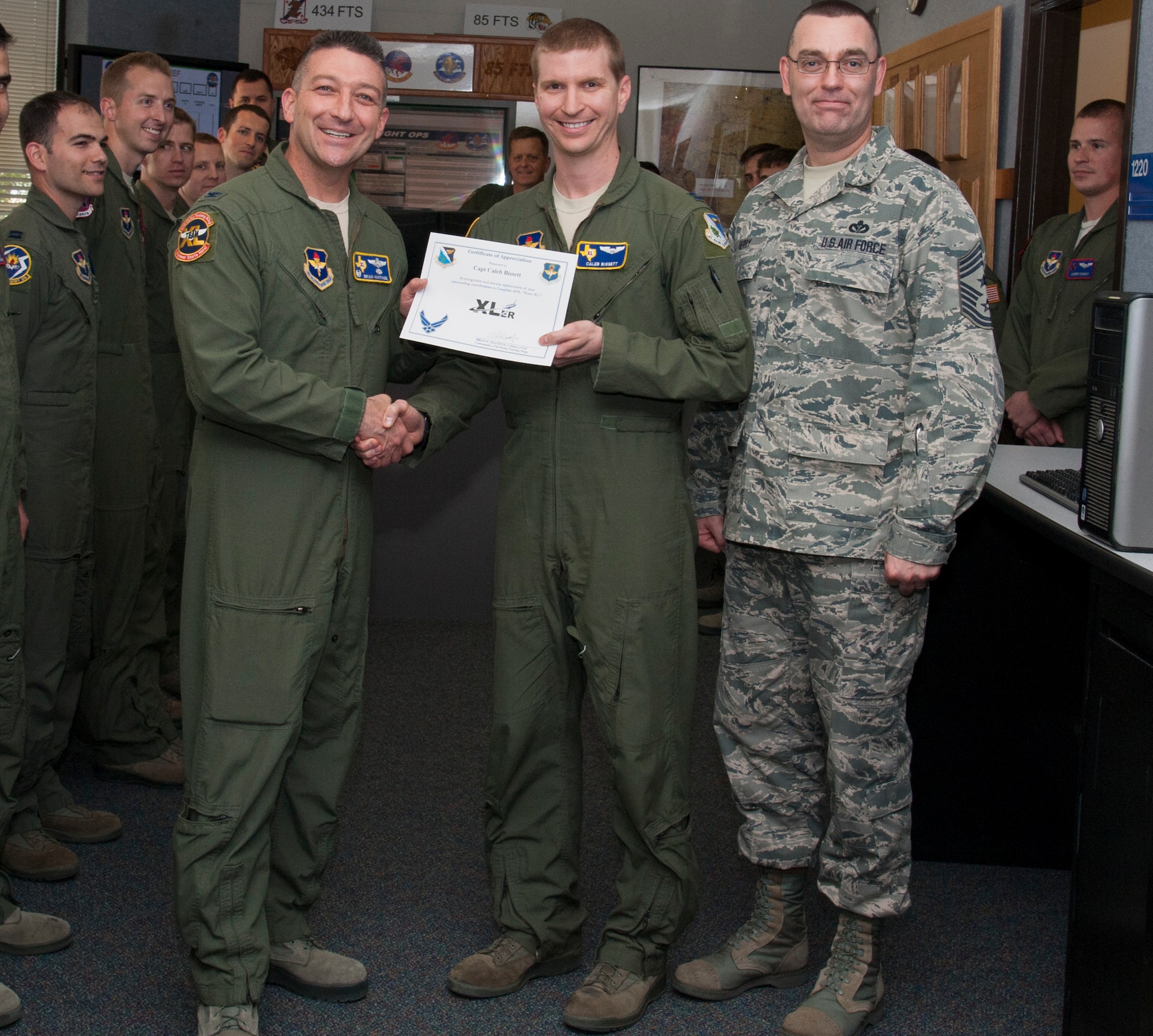Capt. Caleb Bissett, center, 47th Operations Group executive officer and T-6A Texan II instructor pilot, poses with Col. Brian Hastings, left, 47th Flying Training Wing commander, and Chief Master Sgt. Garry Berry, right, 47th FTW command chief, after being presented the XLer of the week award here April 23, 2014. The XLer is a weekly award chosen by wing leadership and given to those who consistently make outstanding contributions to their unit and Laughlin. (U.S. Air Force photo/Airman 1st Class Jimmie D. Pike/Released)