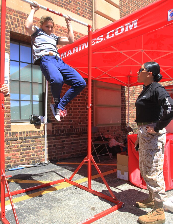Philadelphia -- Sgt. Jerusa Argueta, the enhanced marketing vehicle noncommissioned officer in charge with 1st Marine Corps District, motivates Bianca Reo, a 24-year-old native of Parsippany, N. J., and a participant of the Penn Relays, as she attempts the Marine Corps pull-up challenge, April 24. Reo is currently a student at Villanova.  